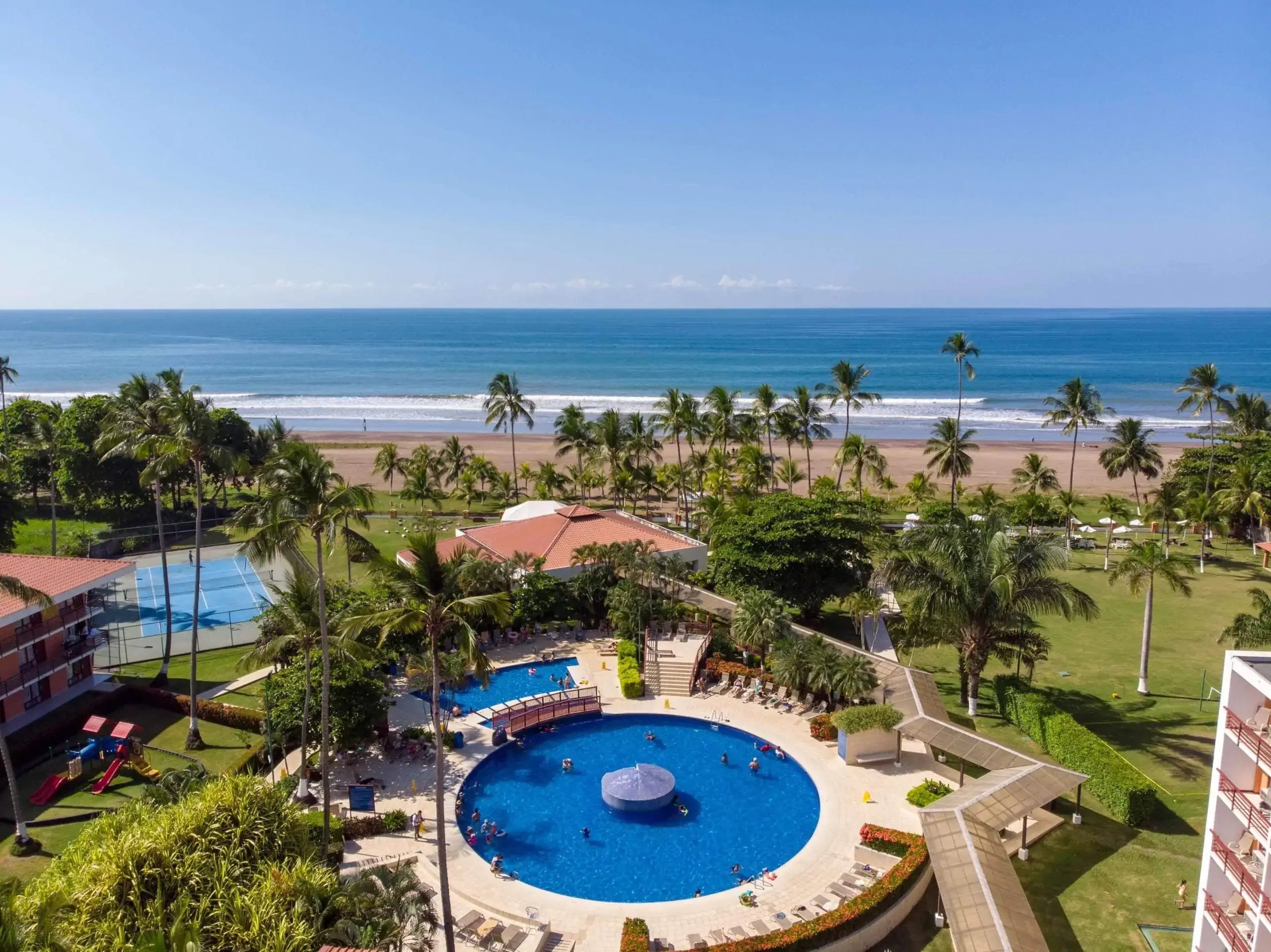 Ariel photo of affordable resort Best Western Jaco Beach with palm trees, views of the ocean, a pool and tennis court.