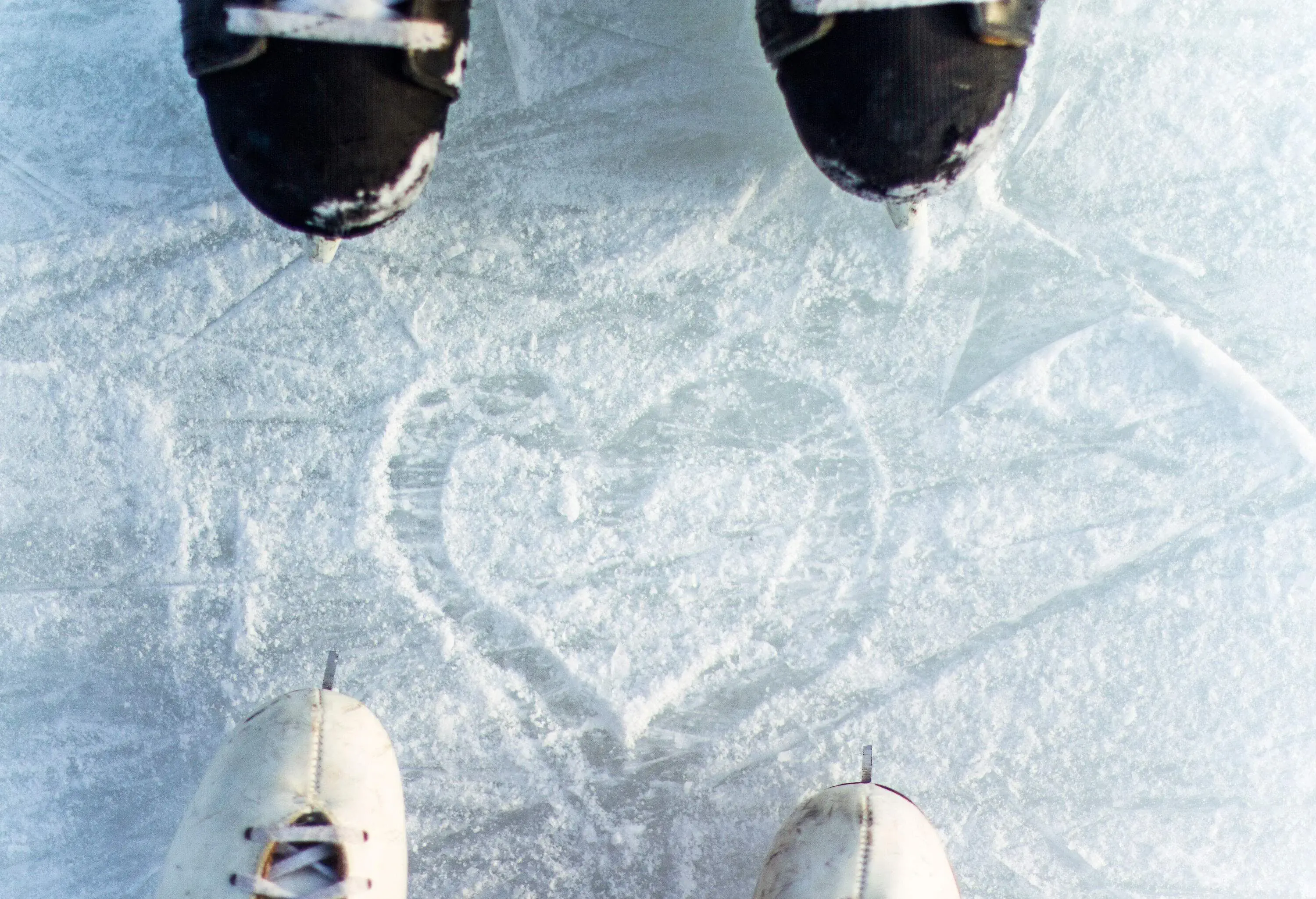 A heart shape is etched into the snow between two pairs of skating shoes.