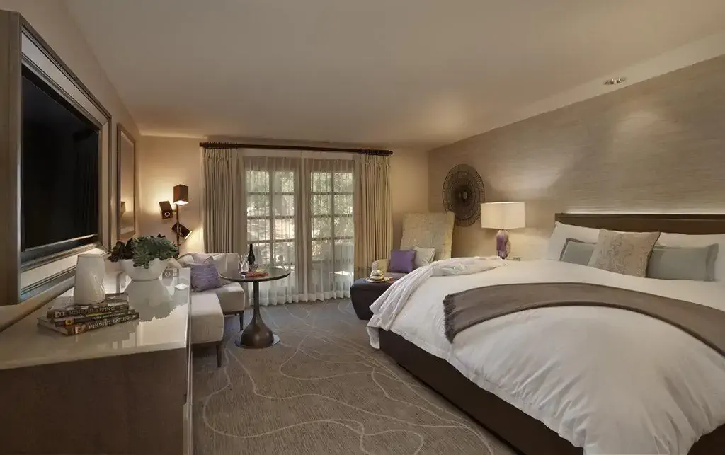 Modern hotel room with large bed, side seating area, TV, and balcony access.