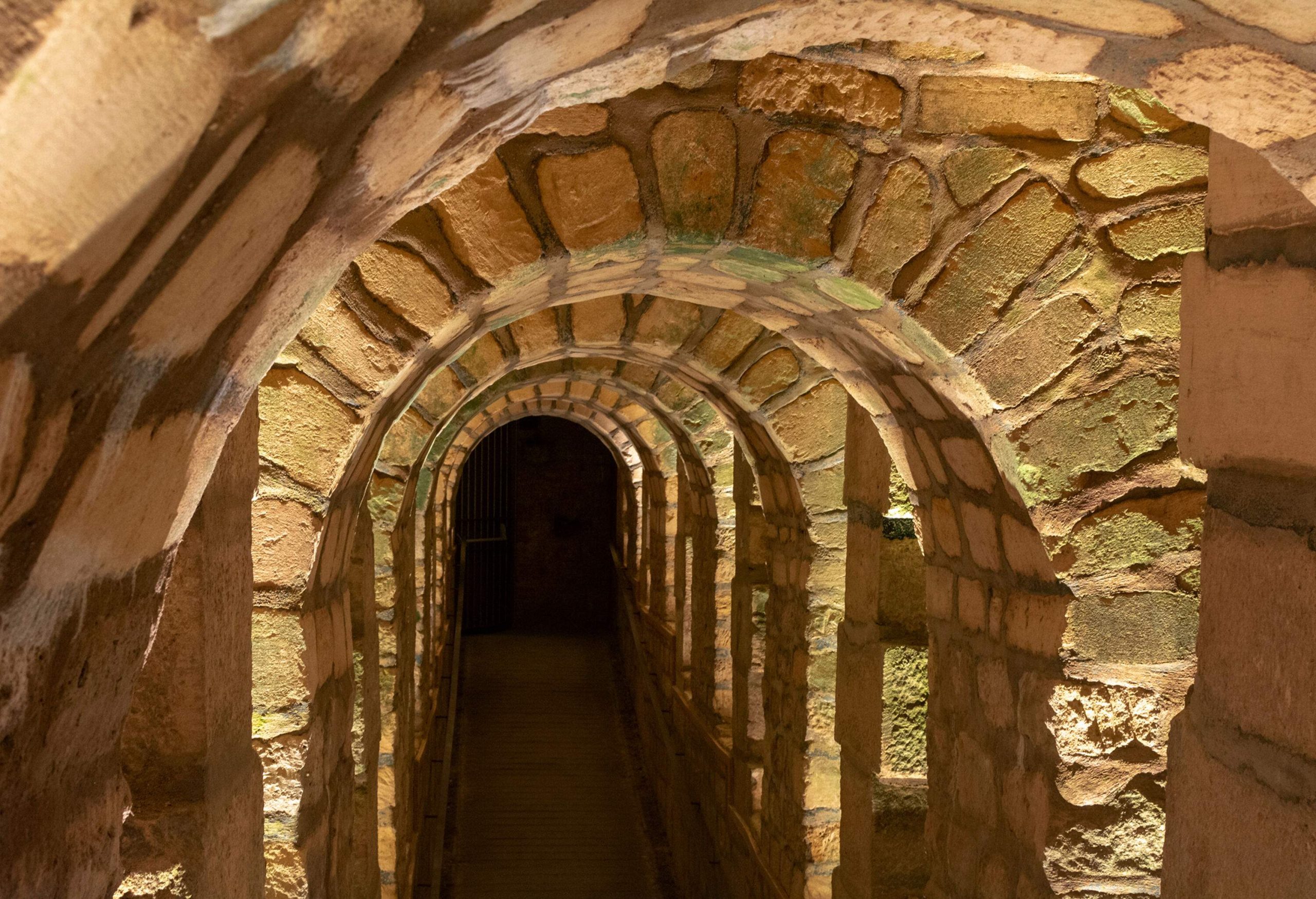 A row of stone arches in a tunnel inside a catacombs.