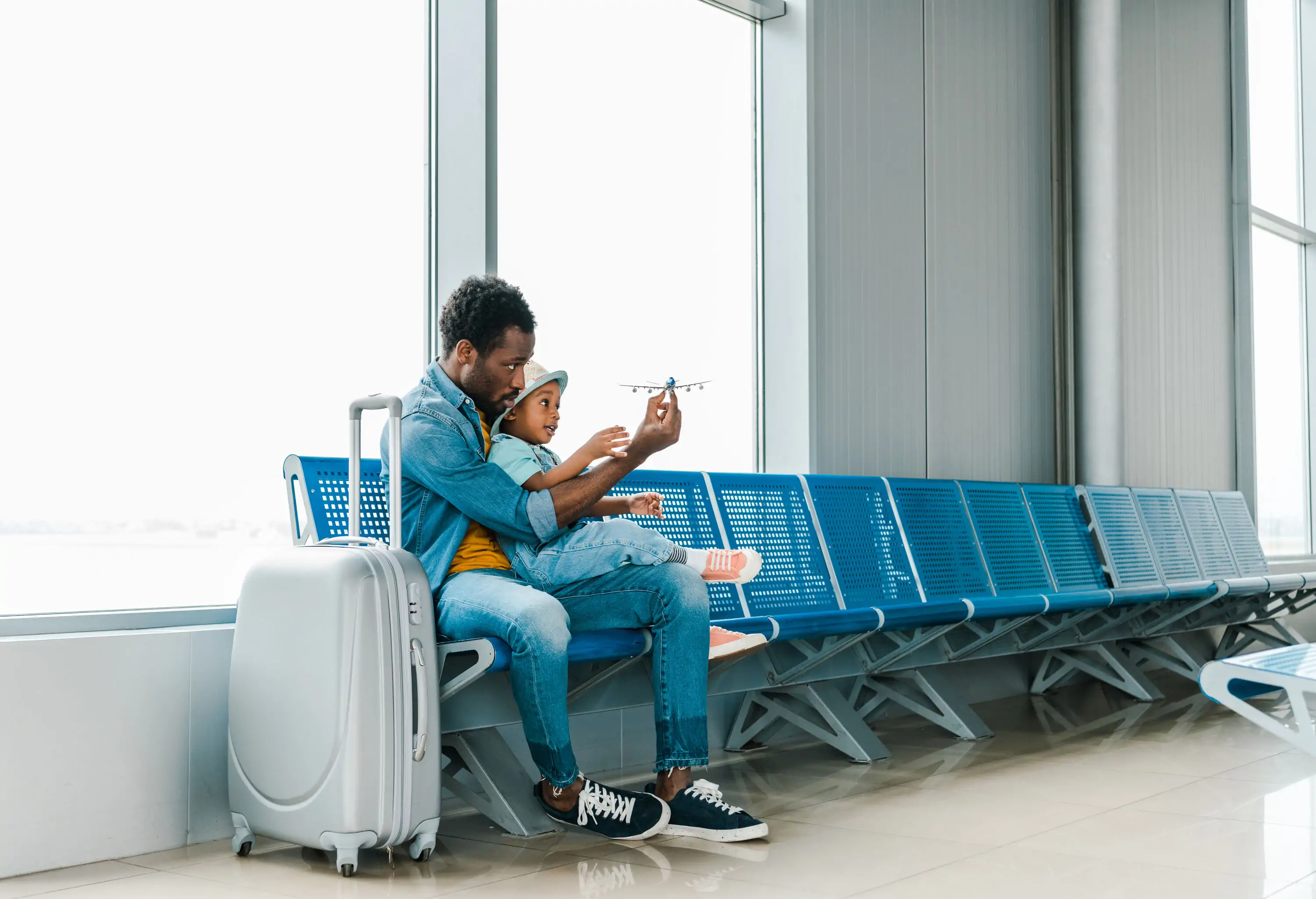 Man sits on a bench with a kid on his lap while playing with a toy plane.