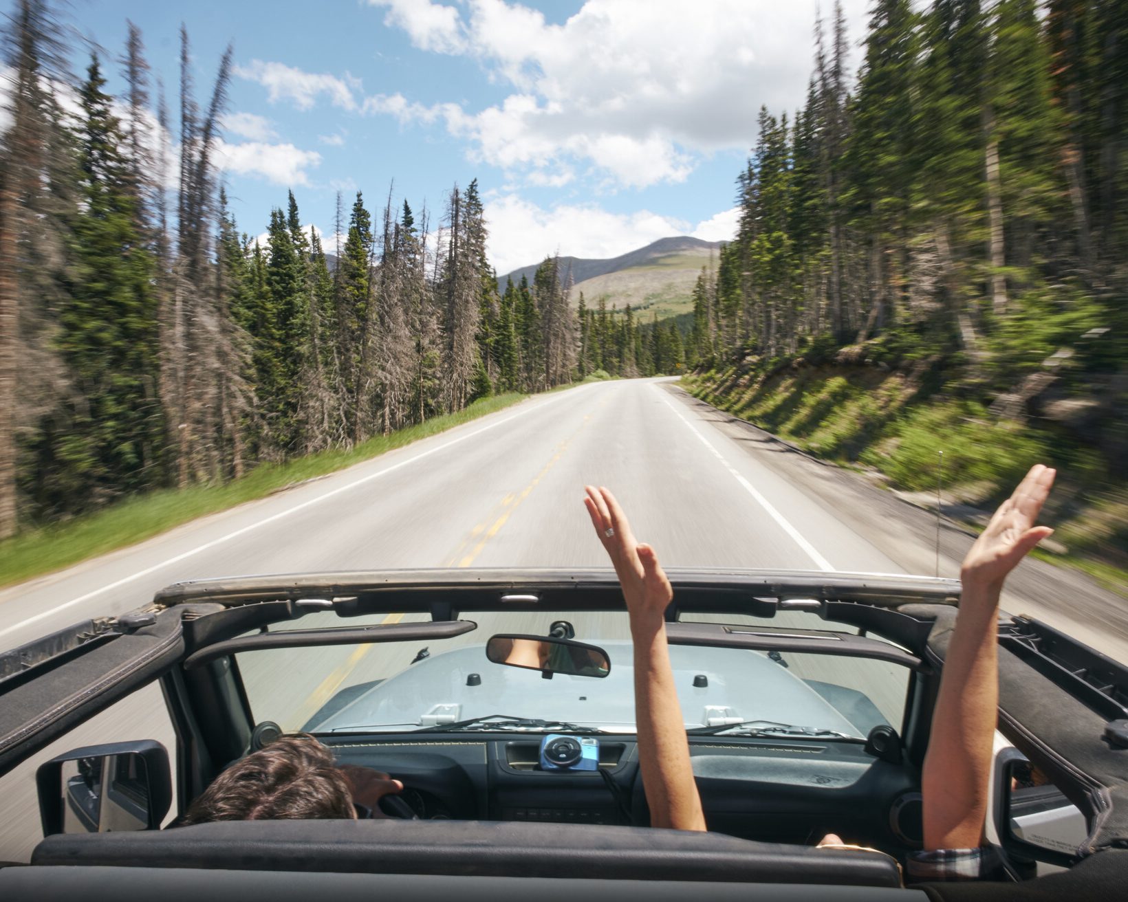 A man in the passenger seat stretching his arms over his head as they drive down the road.