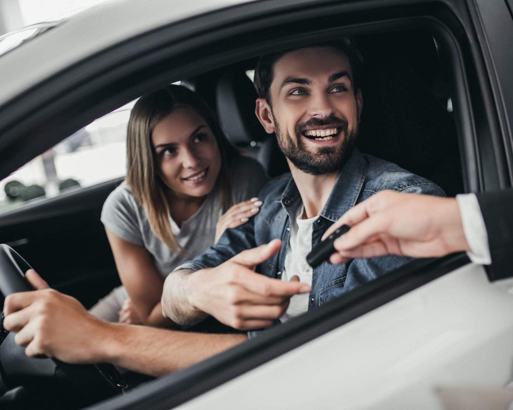 Two happy individuals inside a car look out the driver