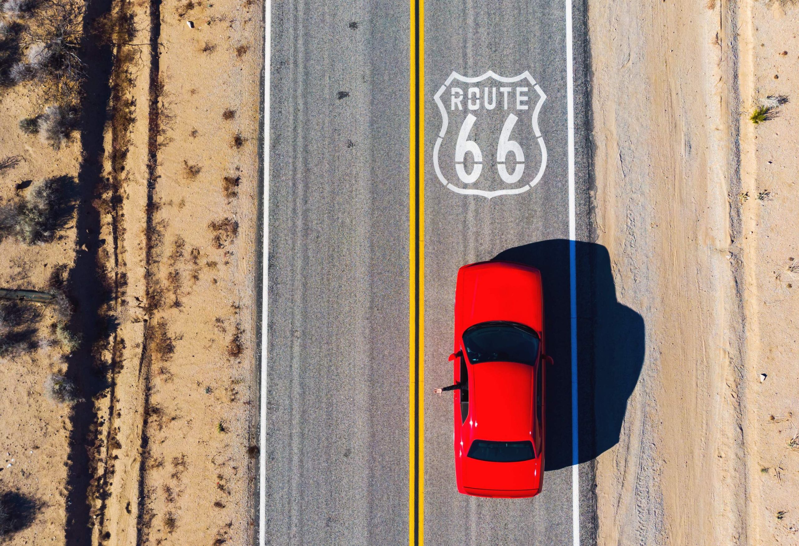 A red car driving down the Route 66 highway.