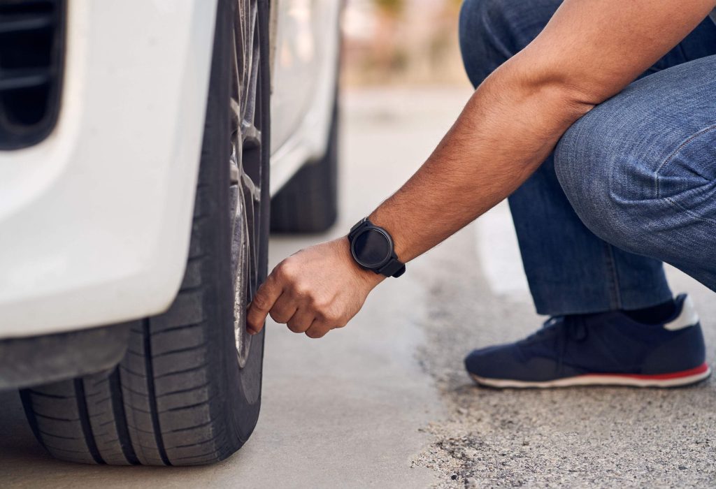 A hand with a black watch checks the tire of a car.