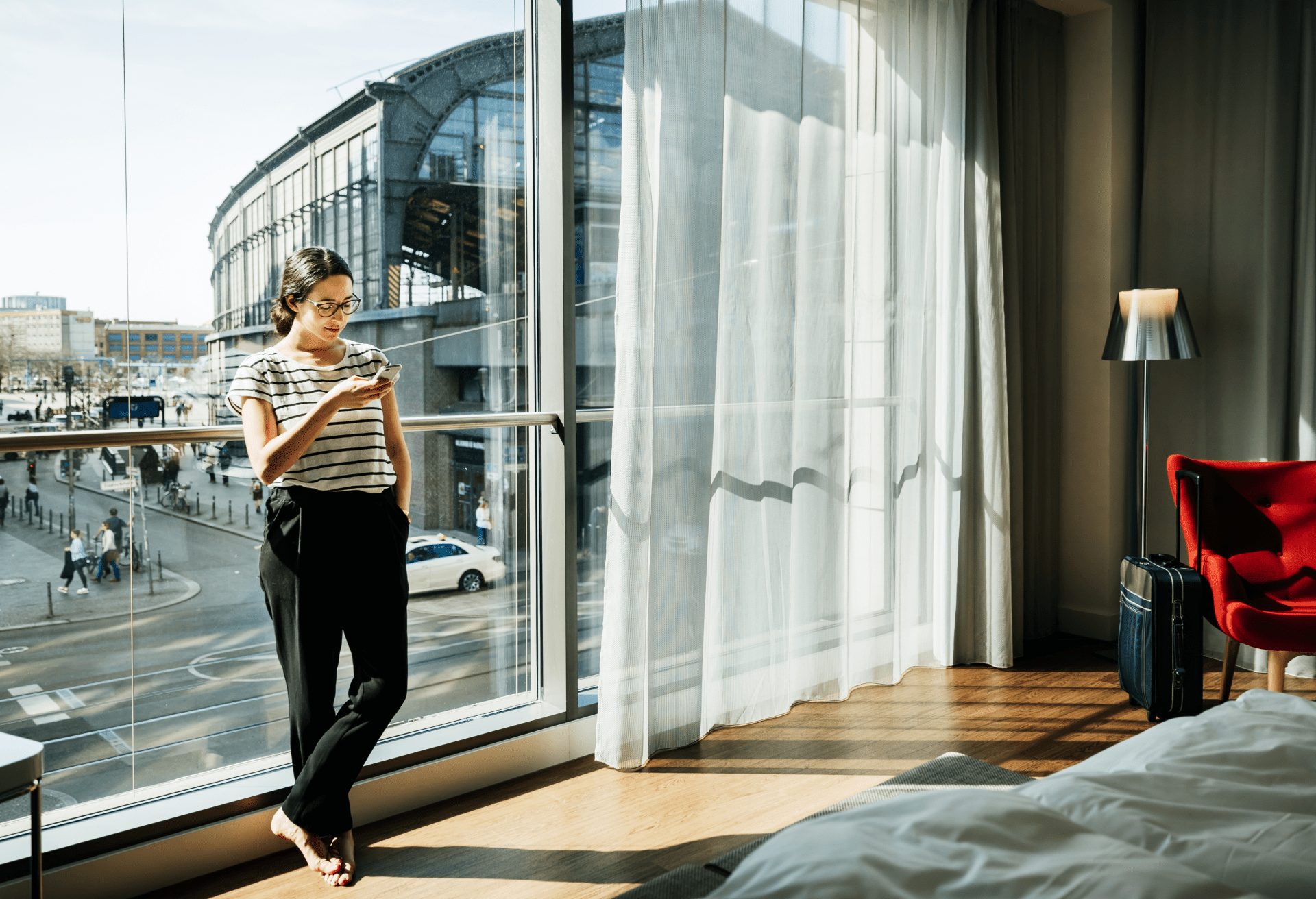 Business traveler leaning against floor to ceiling window of her spacious hotel room.