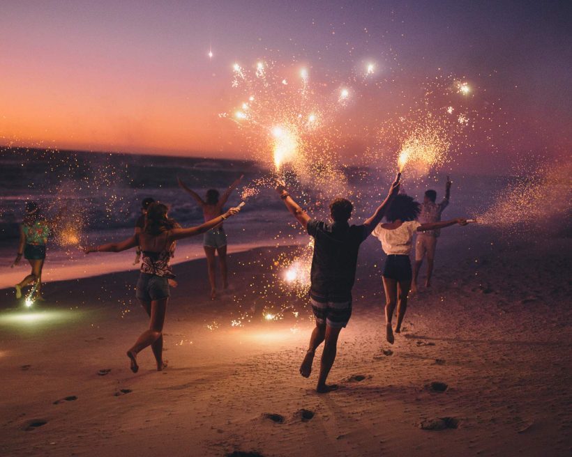 A group of people run with sparklers in their hands along the beach.