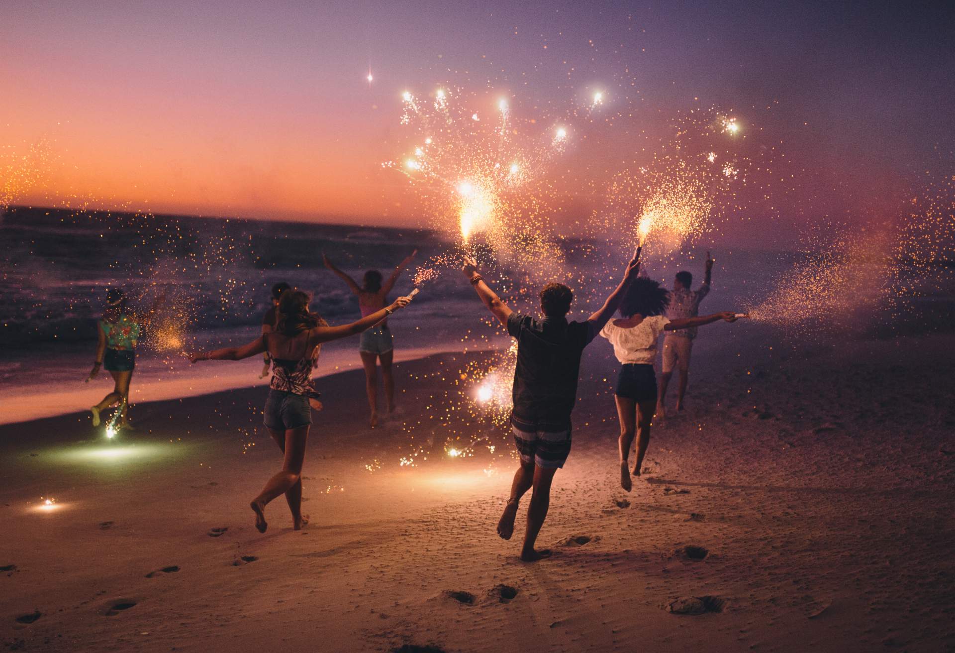 A group of people run with sparklers in their hands along the beach.