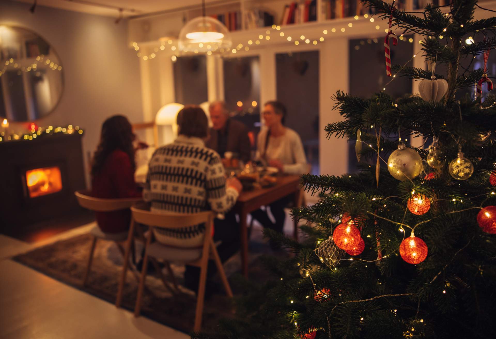 A group of people have dinner next to a decorated Christmas tree.