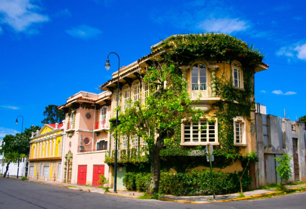 An old mansion along an intersection covered in green vines.