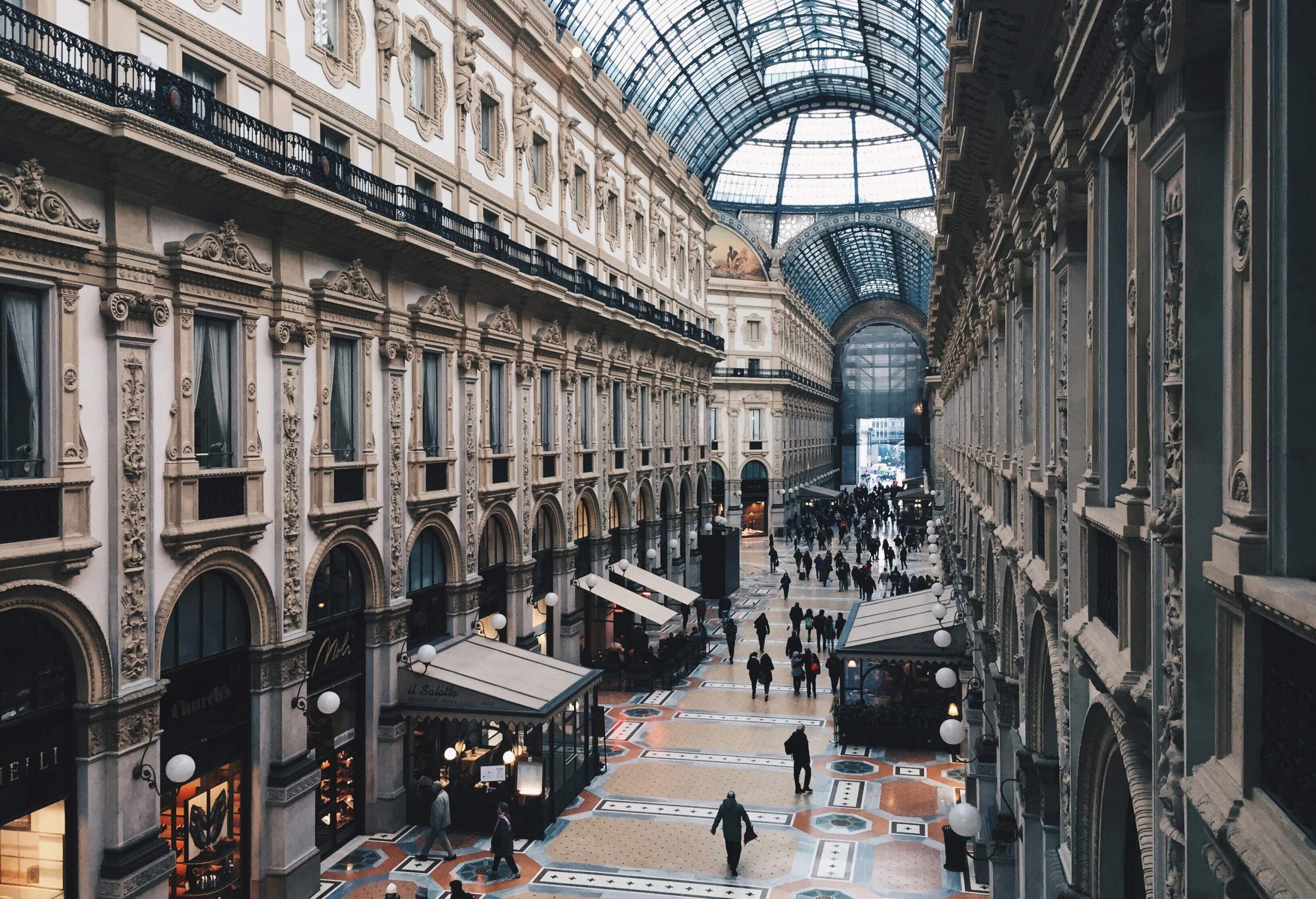A historic mall in Milan boasts a stunning skylight that illuminates the elegant shops and busy crowds of people walking through this architectural masterpiece.