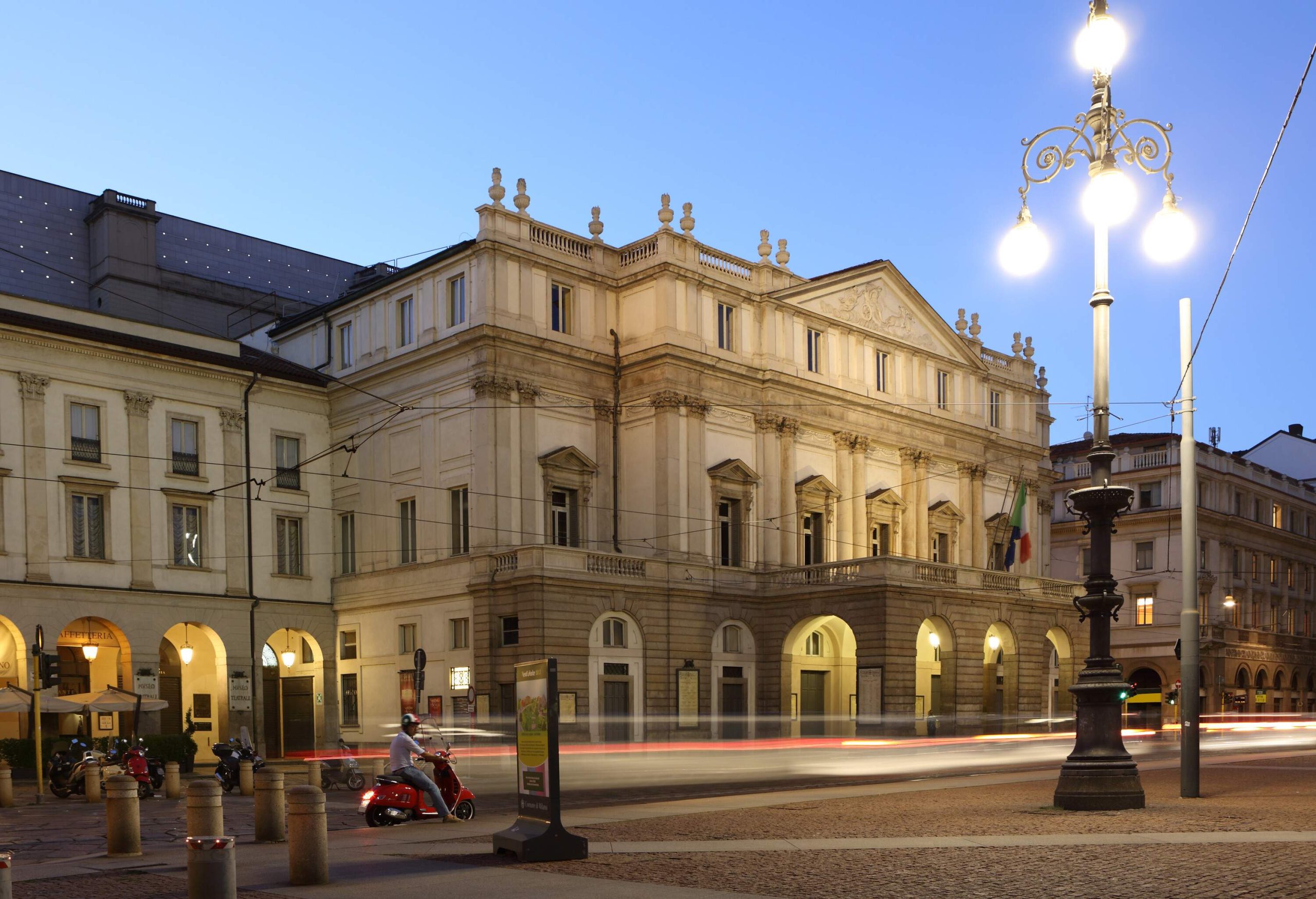 Facade of the famous Teatro alla Scala along a tidy peaceful street with a lighted lamp post.