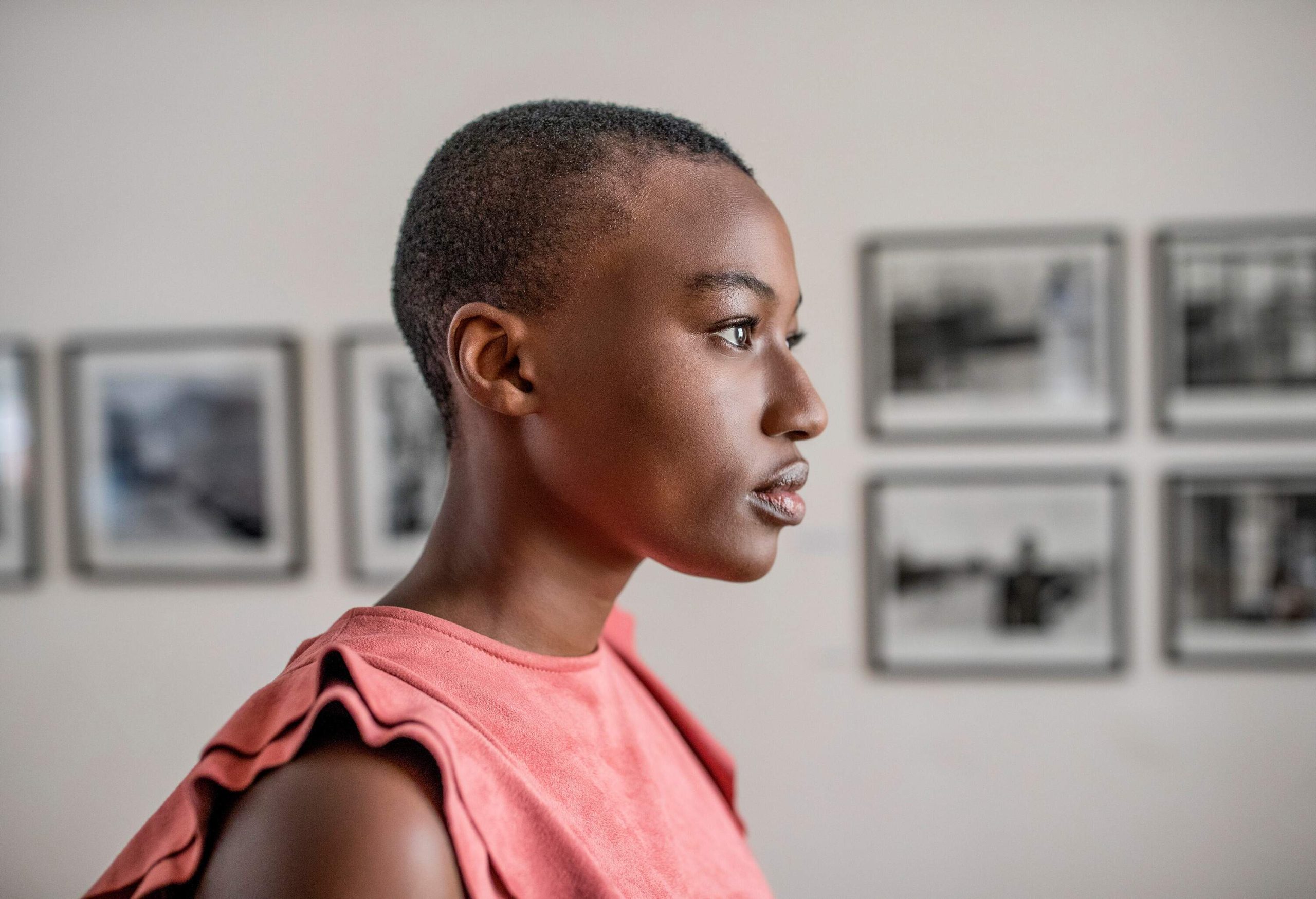 A woman with shaved head walks past the framed photos on a wall.