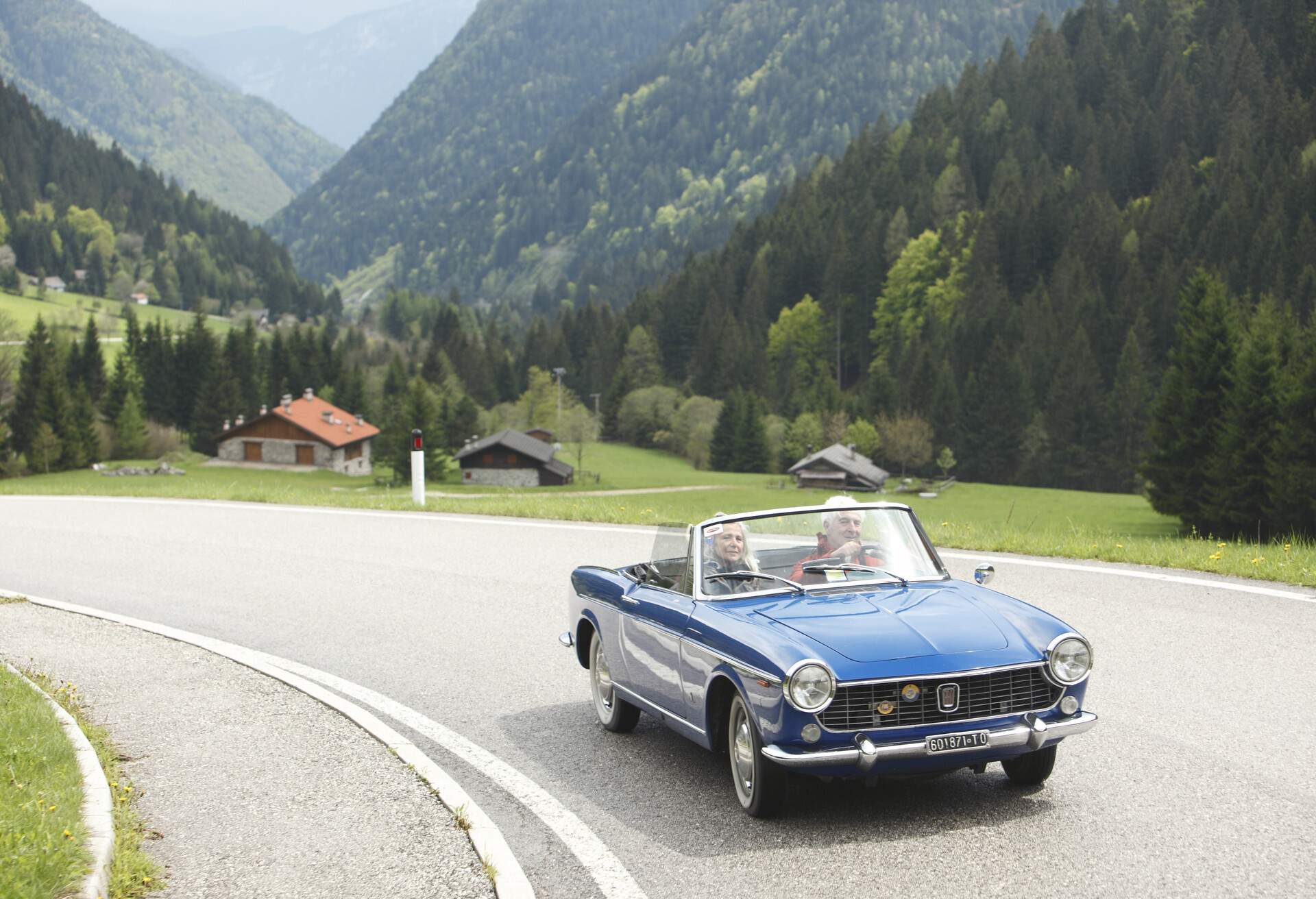 A couple is driving a convertible car on a mountain road