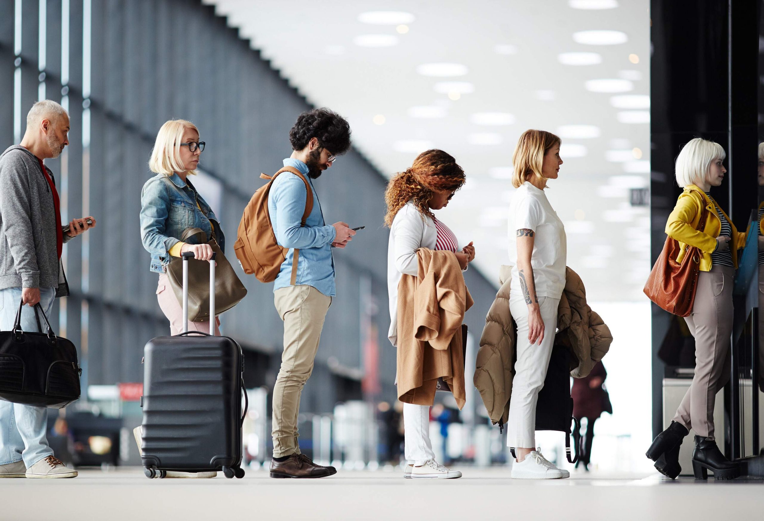Travellers with their luggage lined up at the check-in counters in the airport hall.