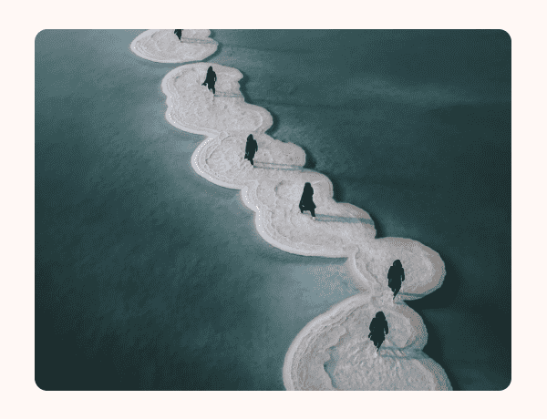 People in all black walking on sand bars in the ocean.