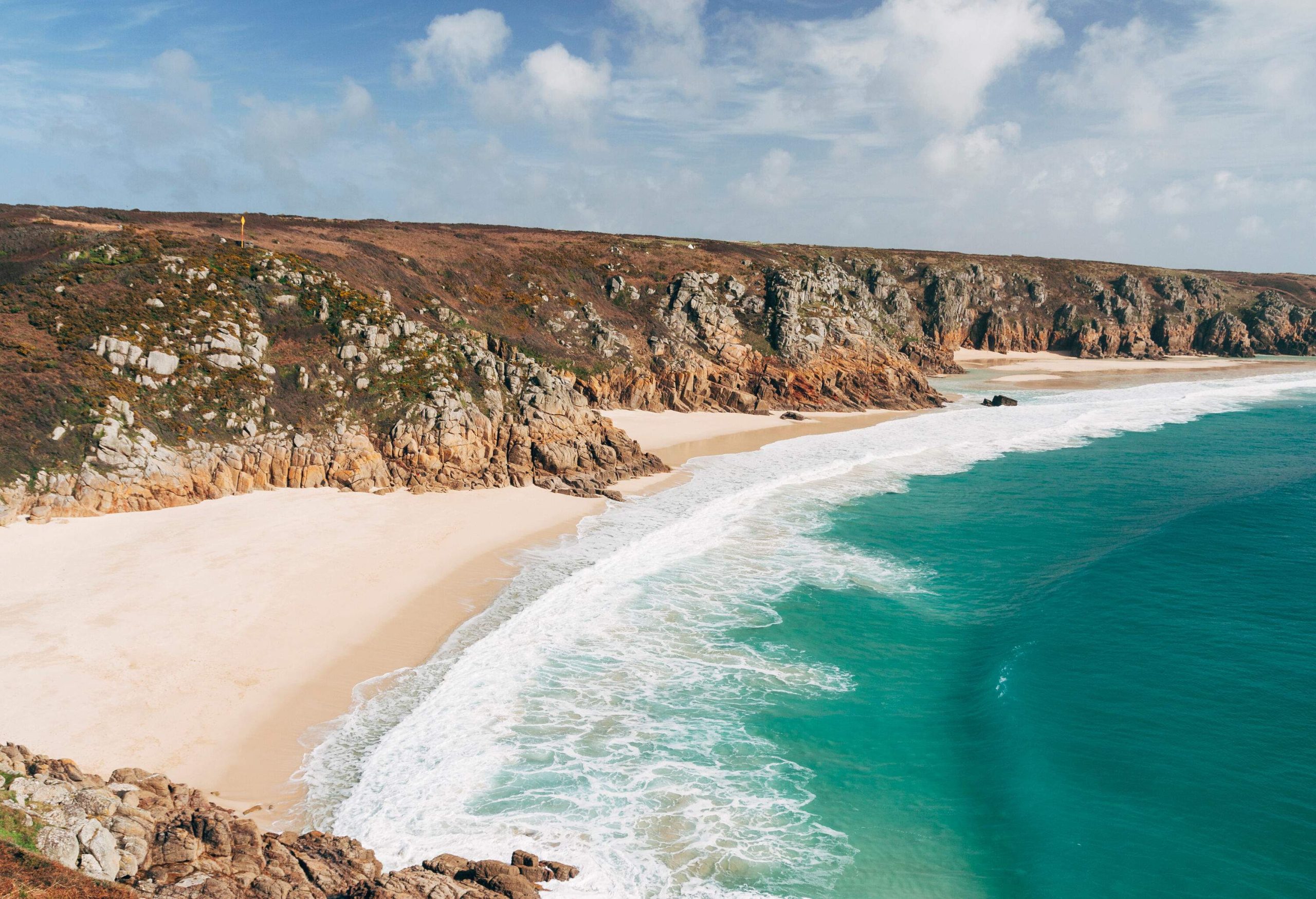 White sea foams splashing up on a sandy shore bordered with low cliffs.