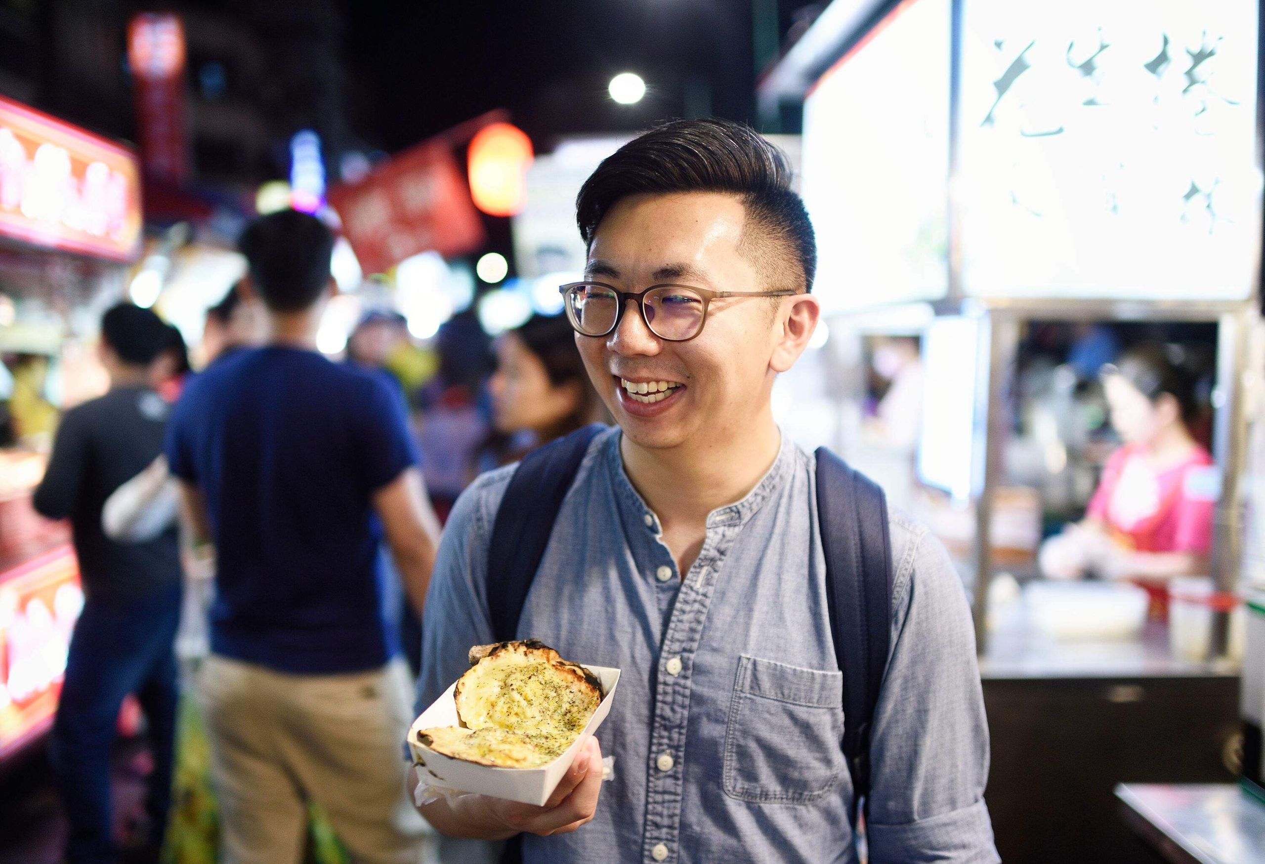 Smiling man holding street food at a night market