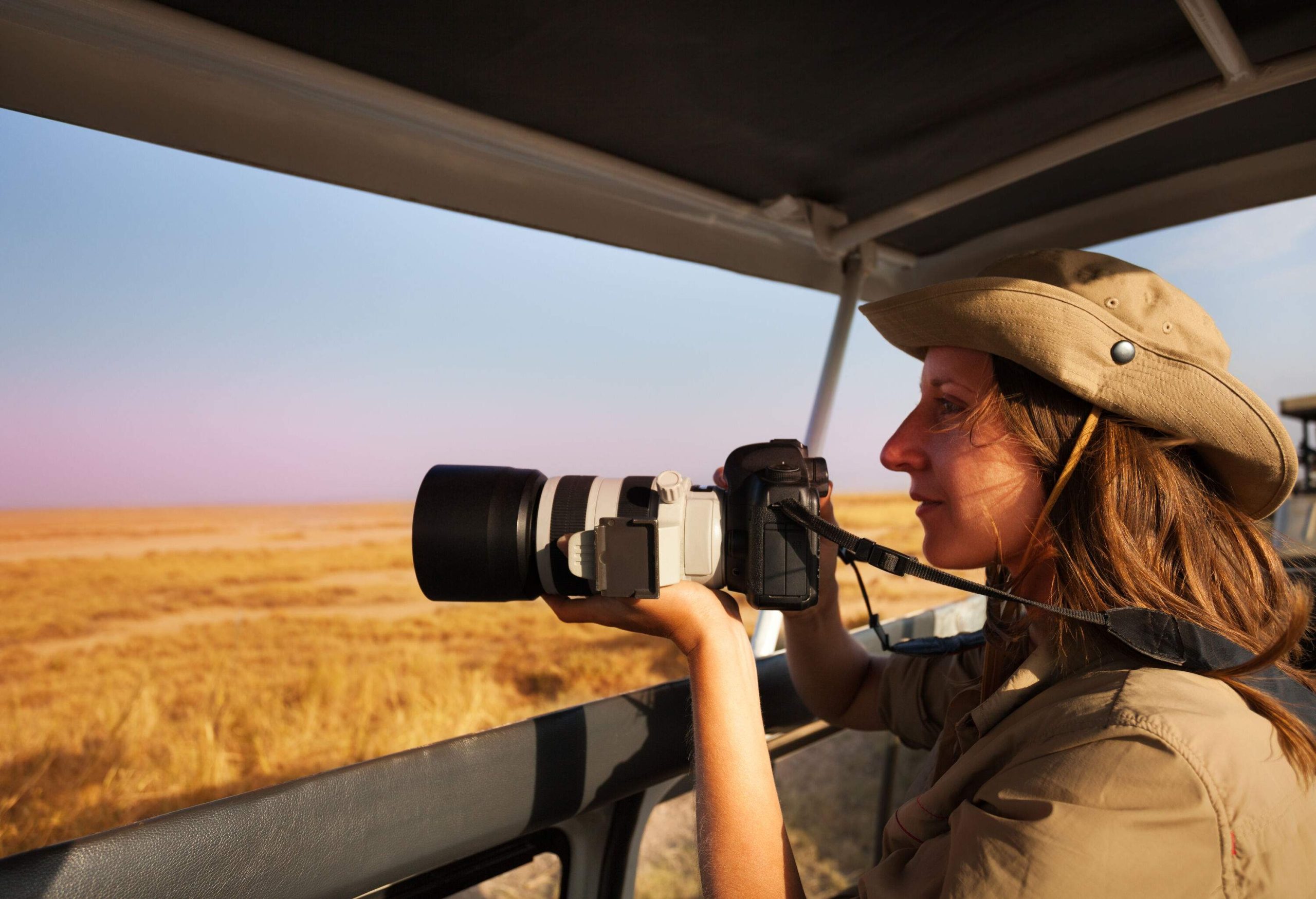 A woman captures a stunning photo from aboard a safari jeep, surrounded by the vast expanse of the savannah.
