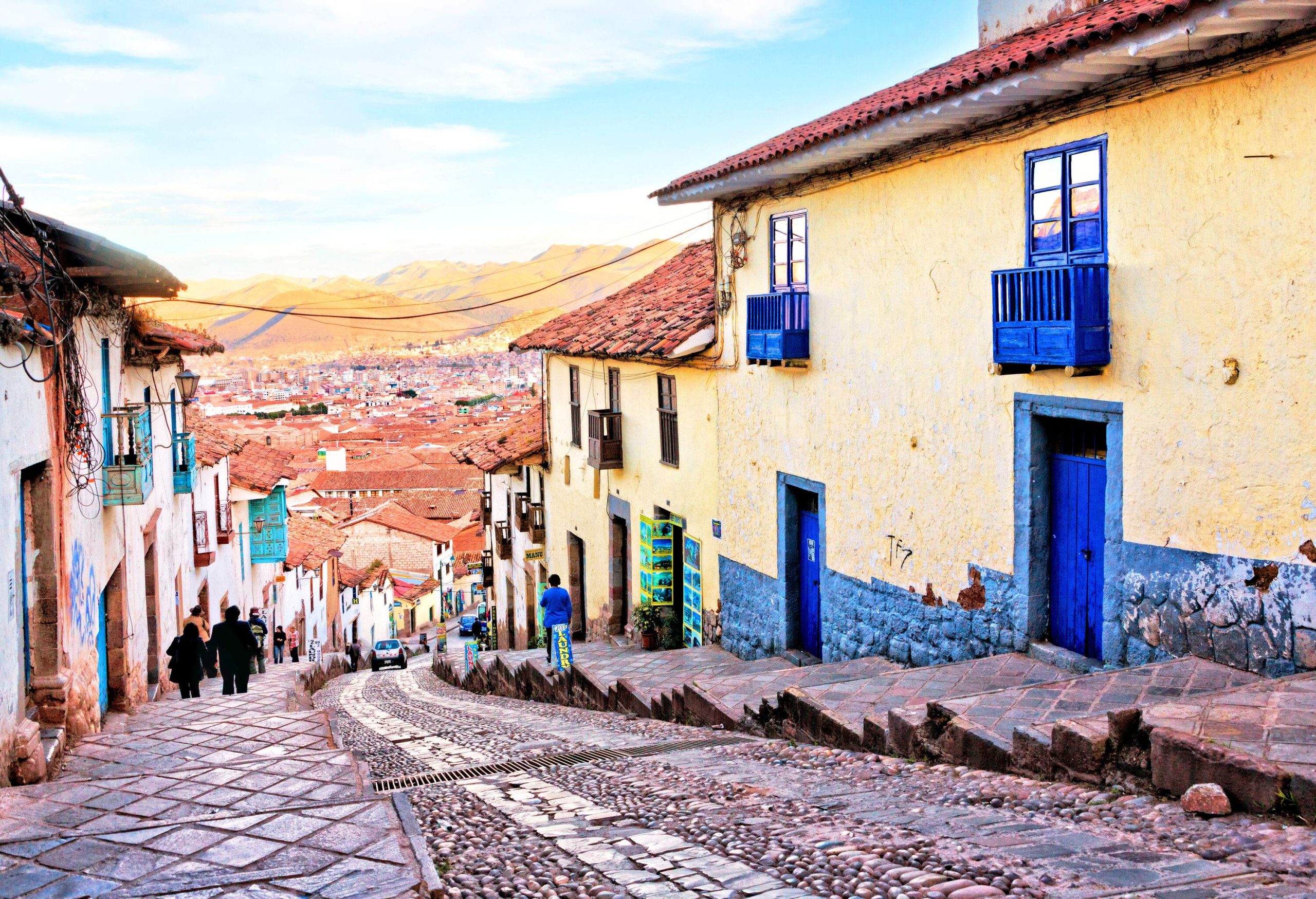 An old village town with people wandering past the buildings along a stone-paved stepped street.