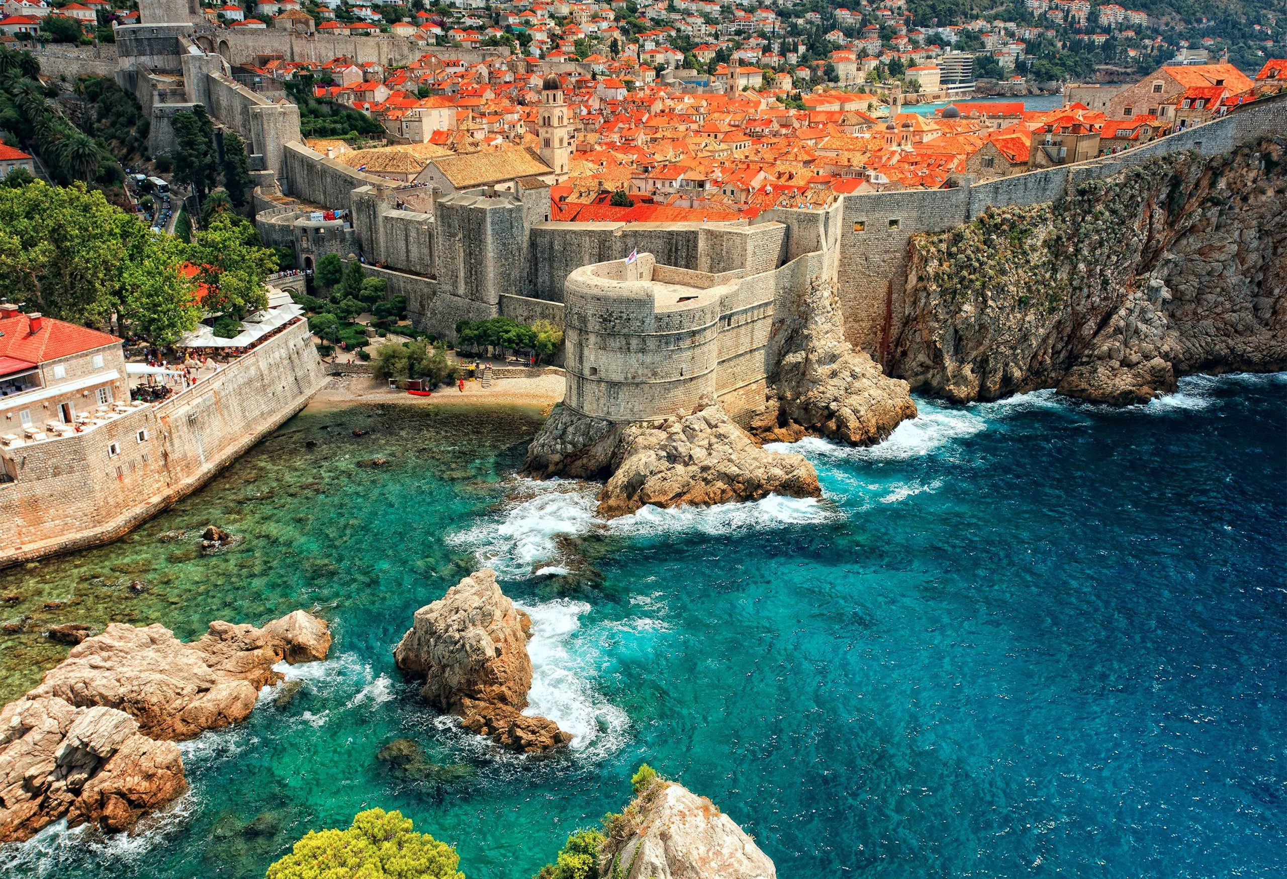 A cylindrical fortress along the shore linked to the defensive stone walls surrounding the populous city.