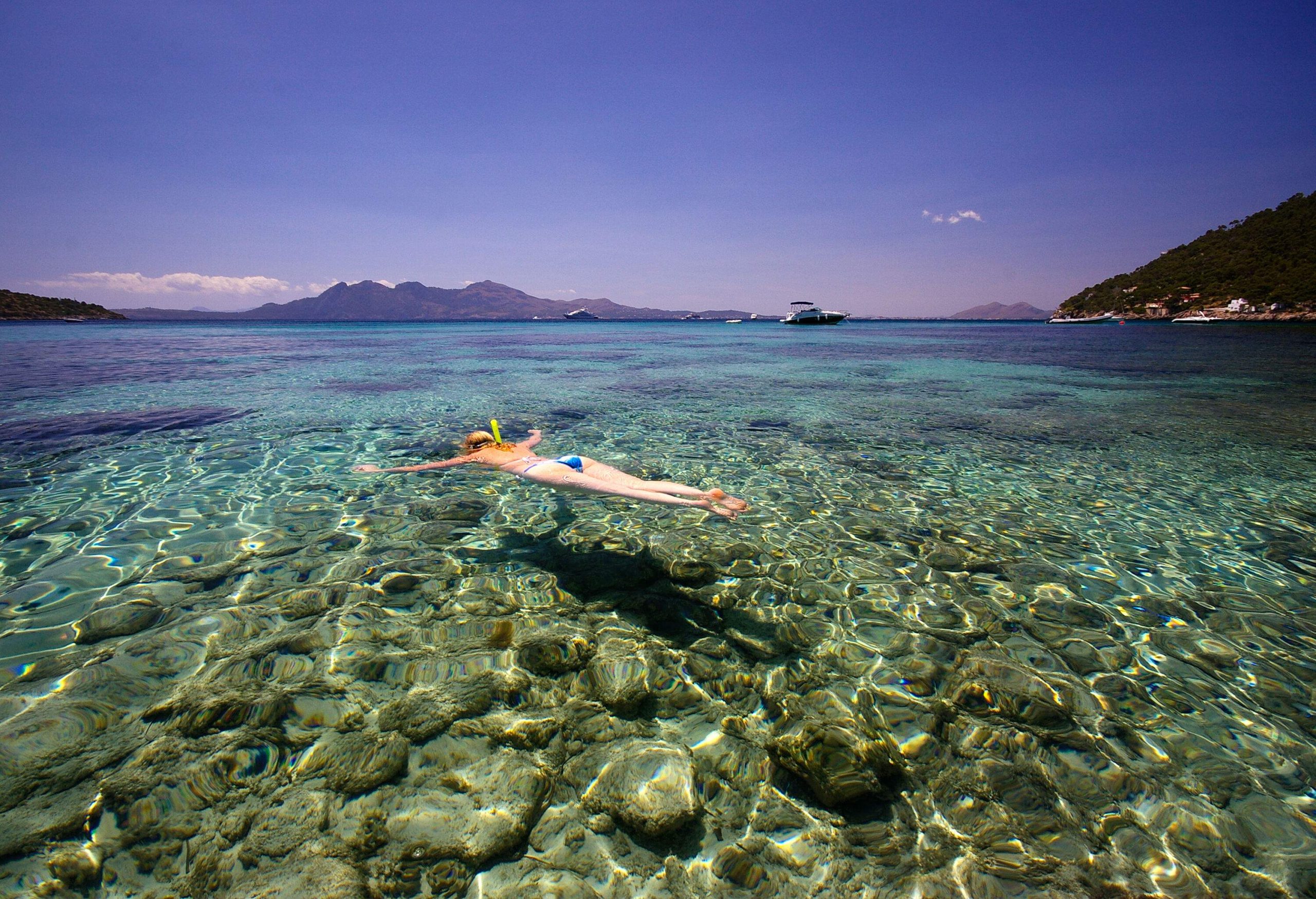 A woman in a bathing suit snorkels across the clear waters of a beach.