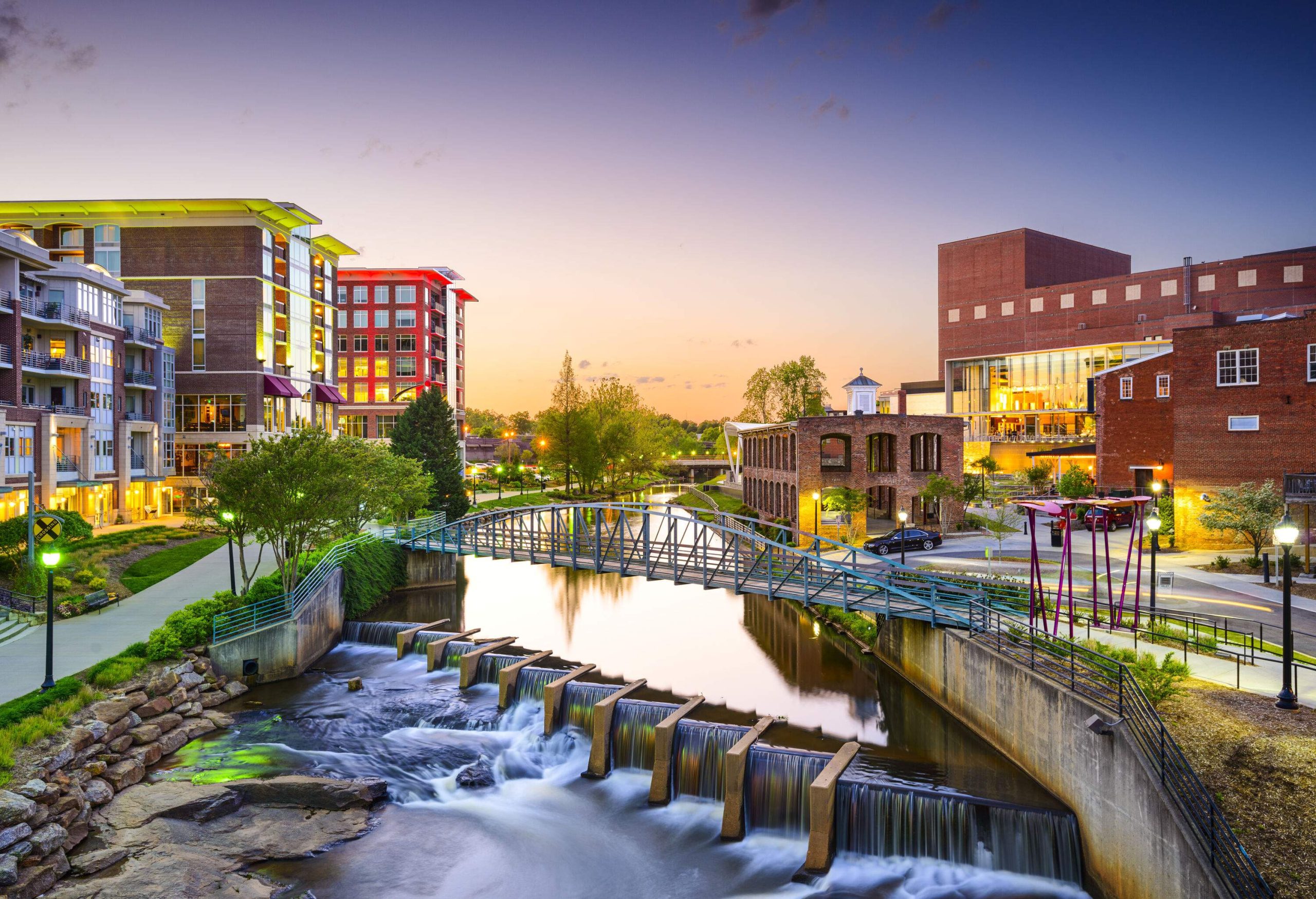 A steel footbridge across a water canal with a dam bordered by a beautiful promenade and modern buildings.