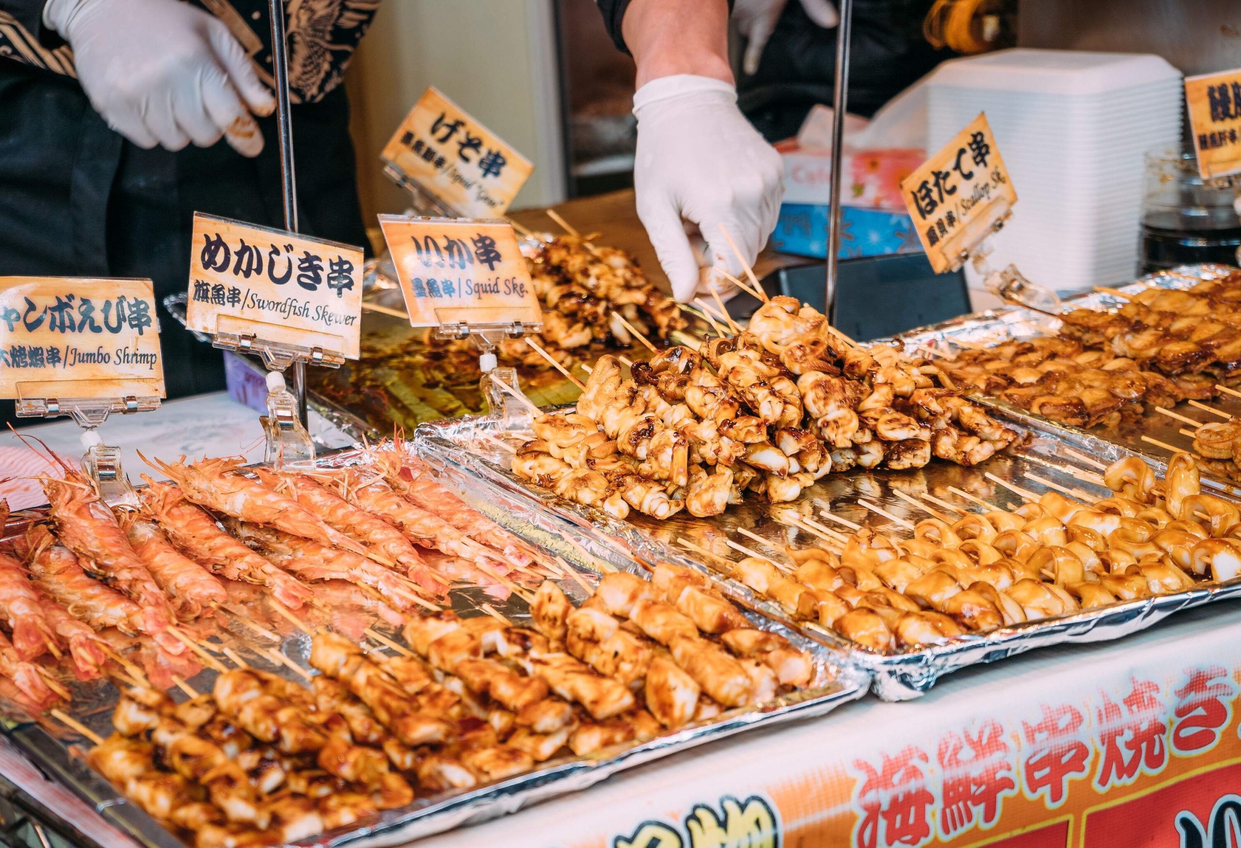 A vendor stall with displays of grilled seafood skewers with labels.