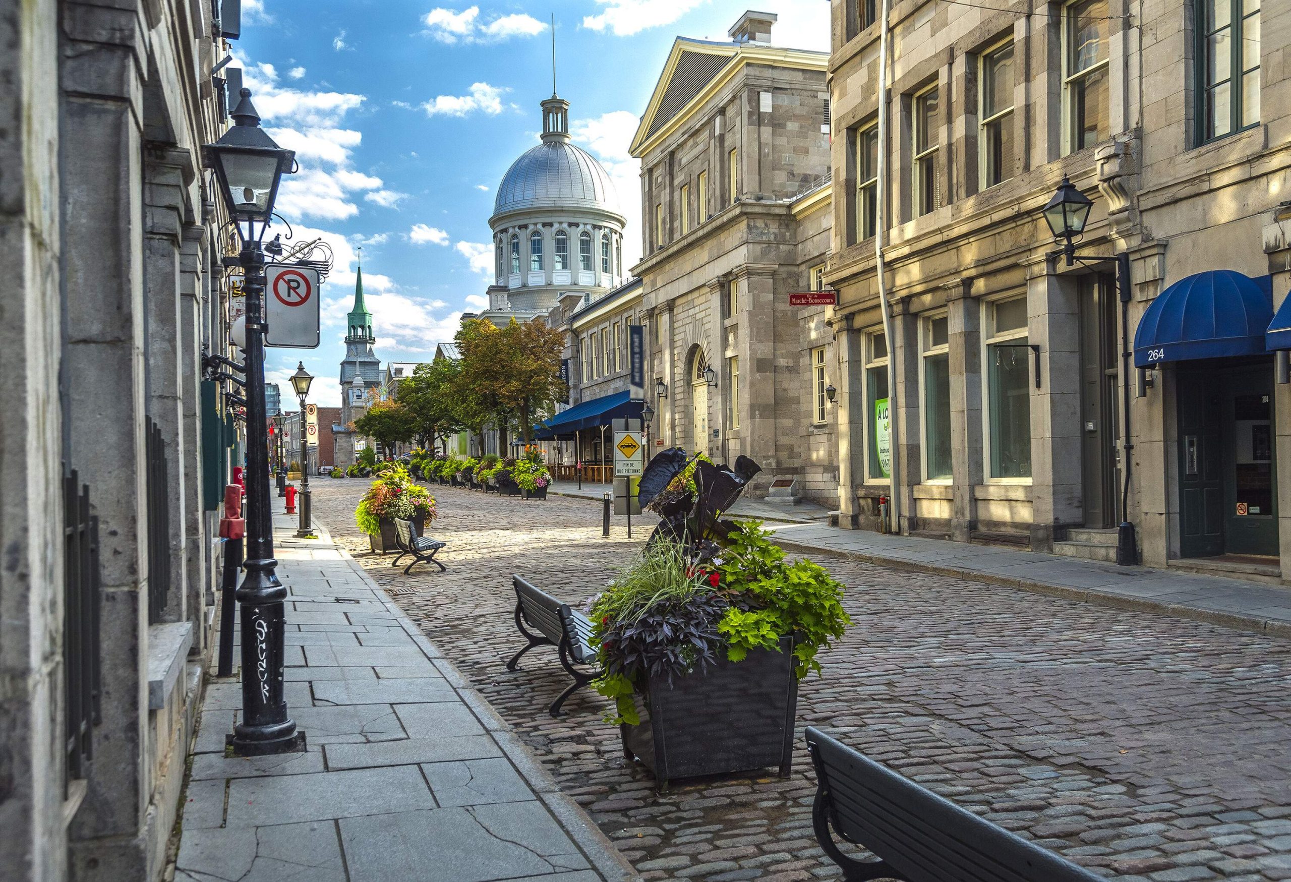 A cobbled street lined with classic buildings against the cloudy blue sky.