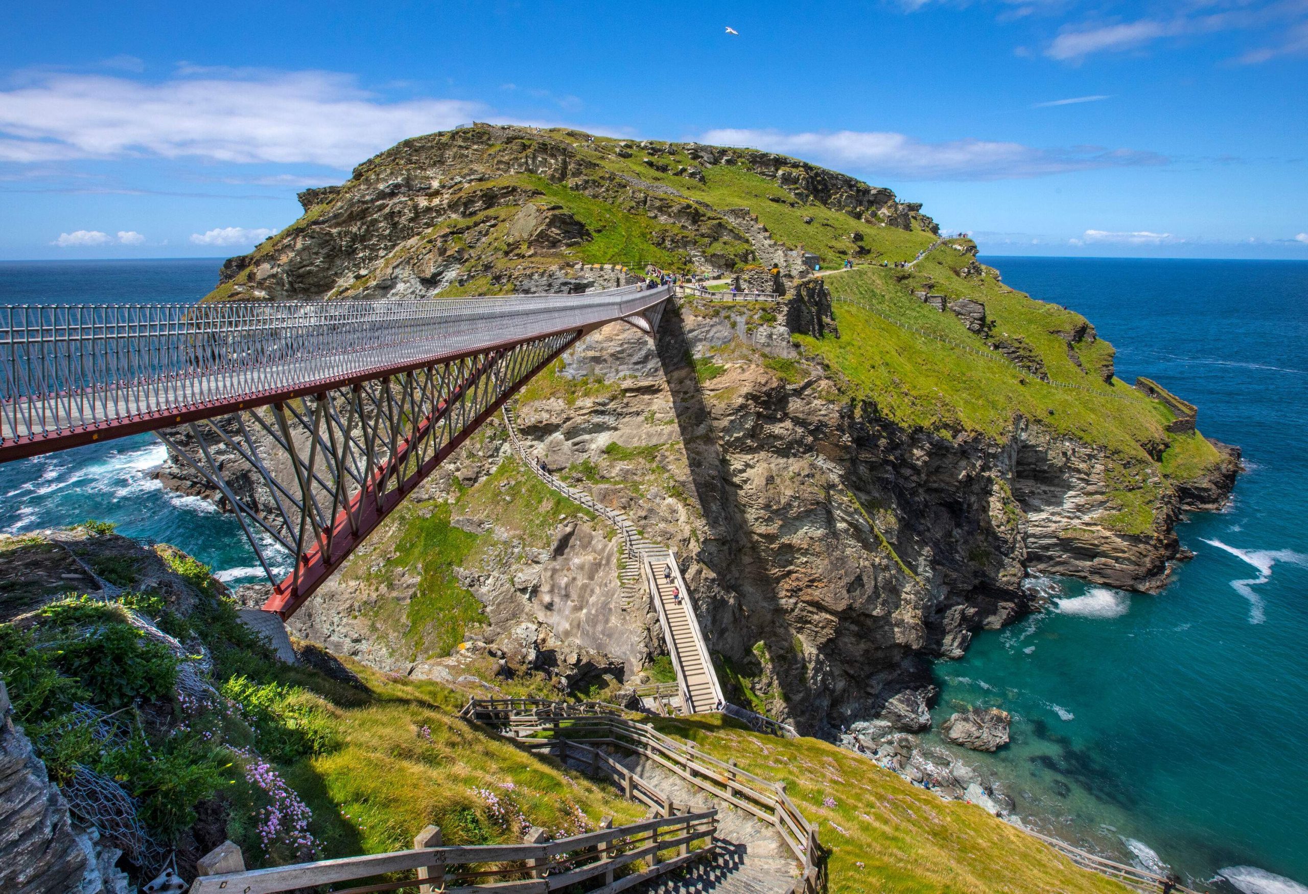 The Tintagel Castle Footbridge elegantly stretches across the rugged cliffs, suspended above the sparkling waters below.