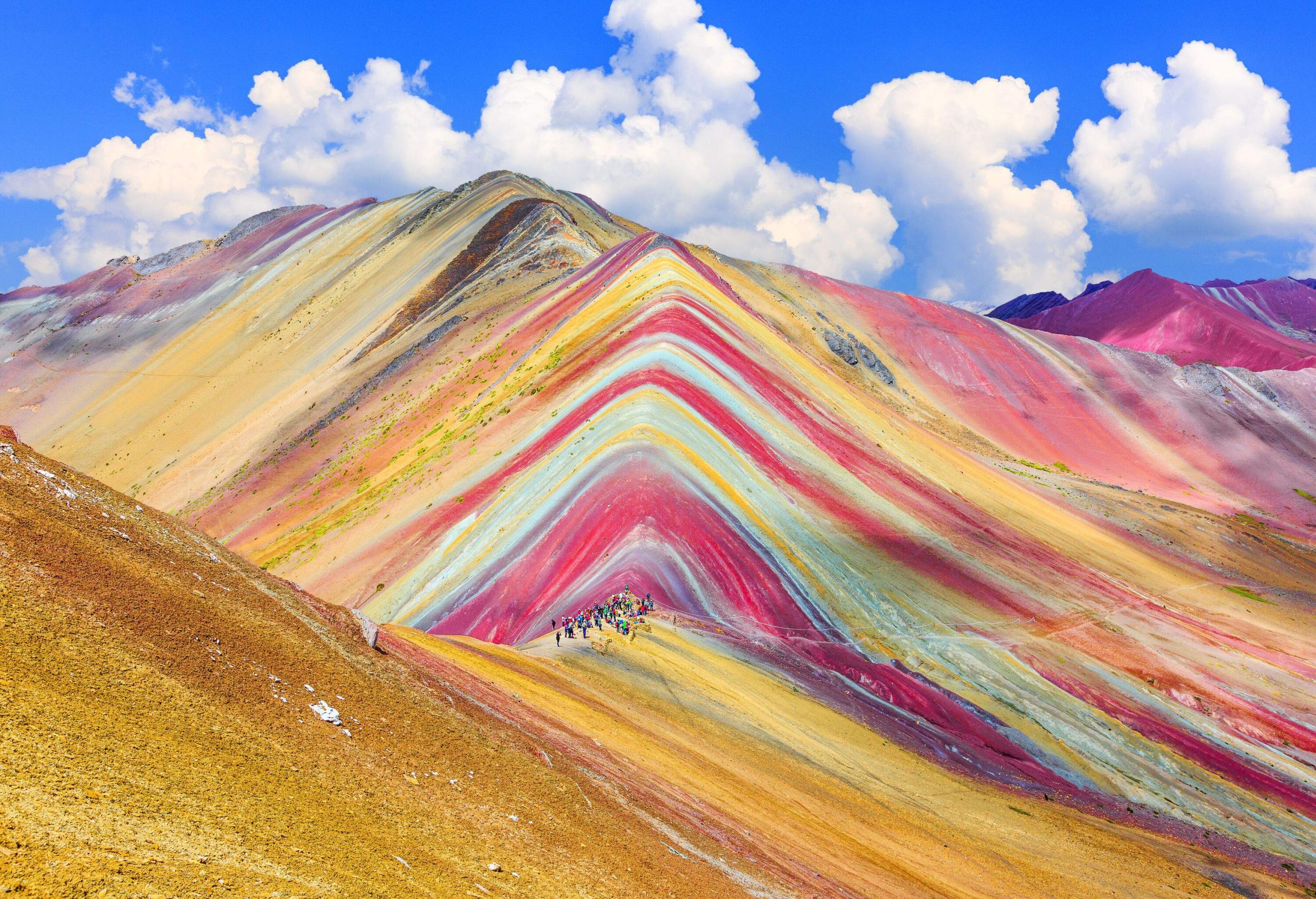 People standing on the colourful ridges of a mountain range.