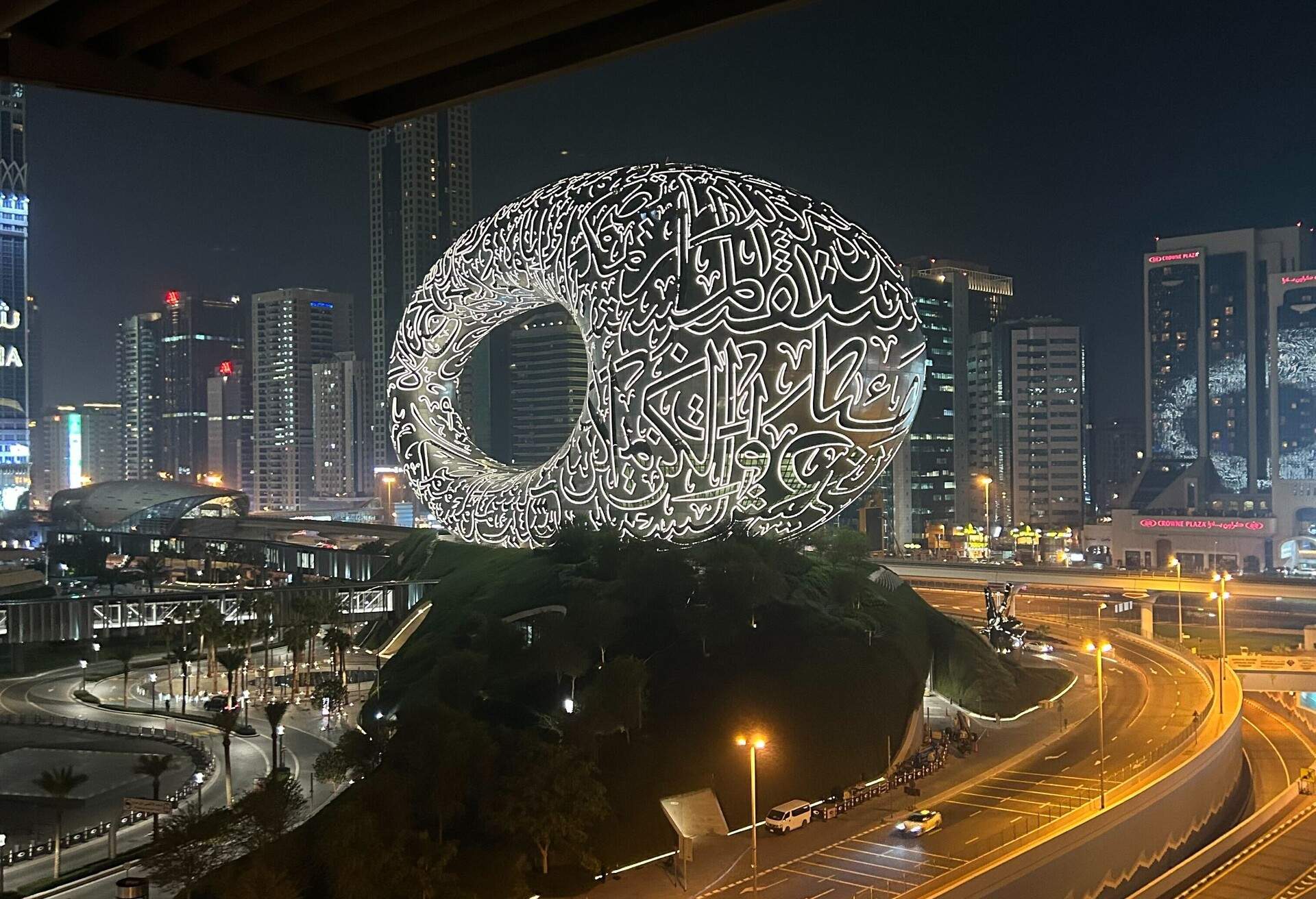 A beautiful monument in the shape of a sphere with Arabic letters written in bright LED lights stands next to a road. 