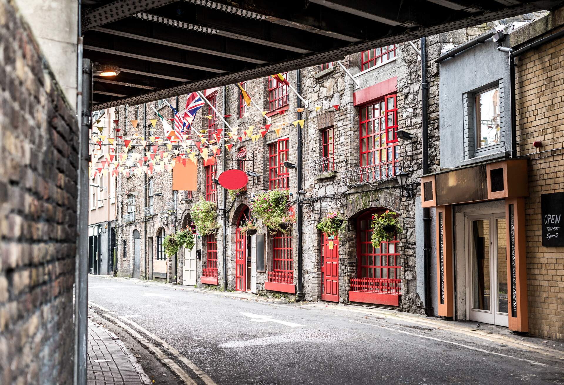 A tiny road lined with brick buildings with stringed holiday decorations.