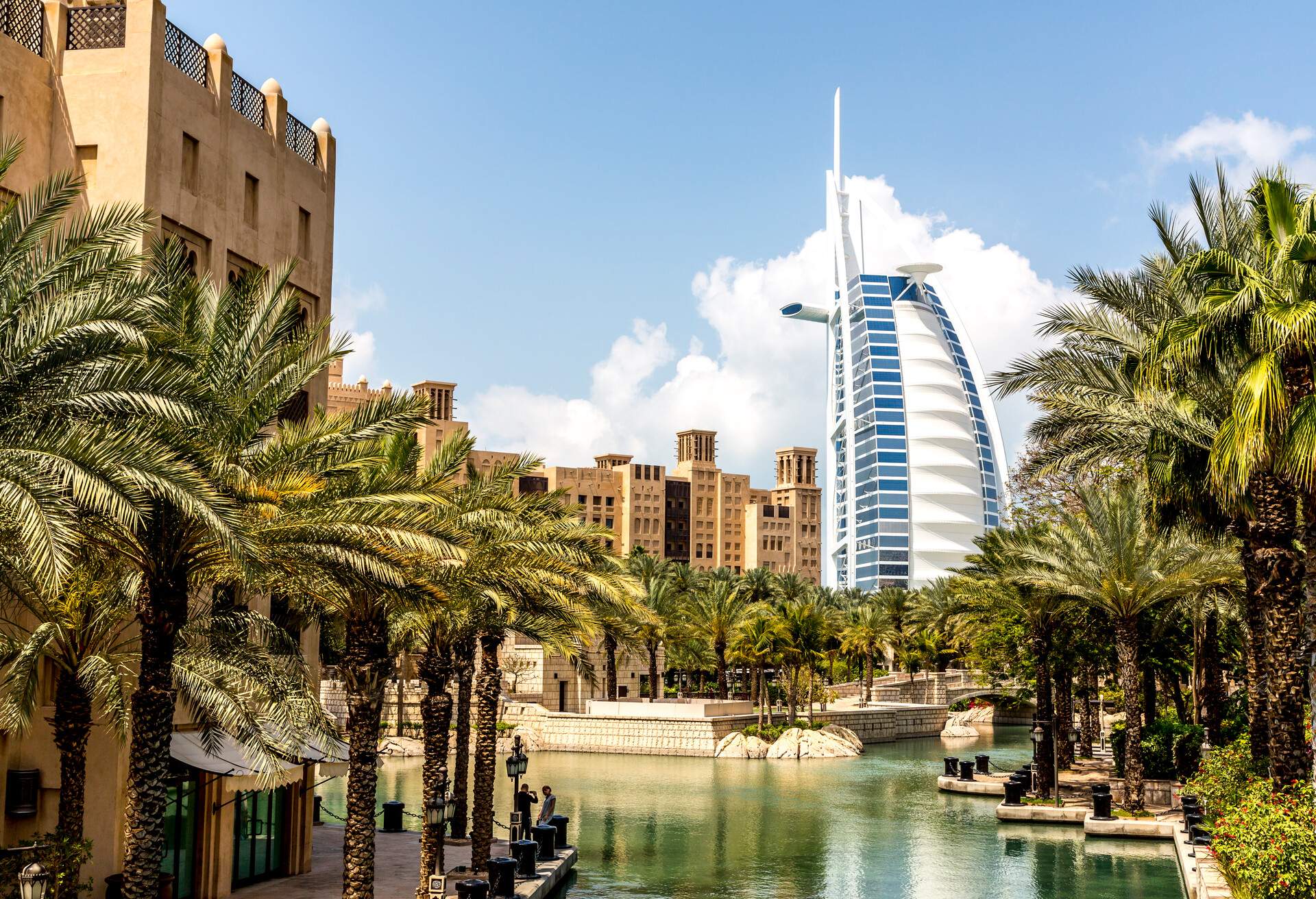 A beautiful park lake bordered by palm trees with the Burj Al Arab in the background.