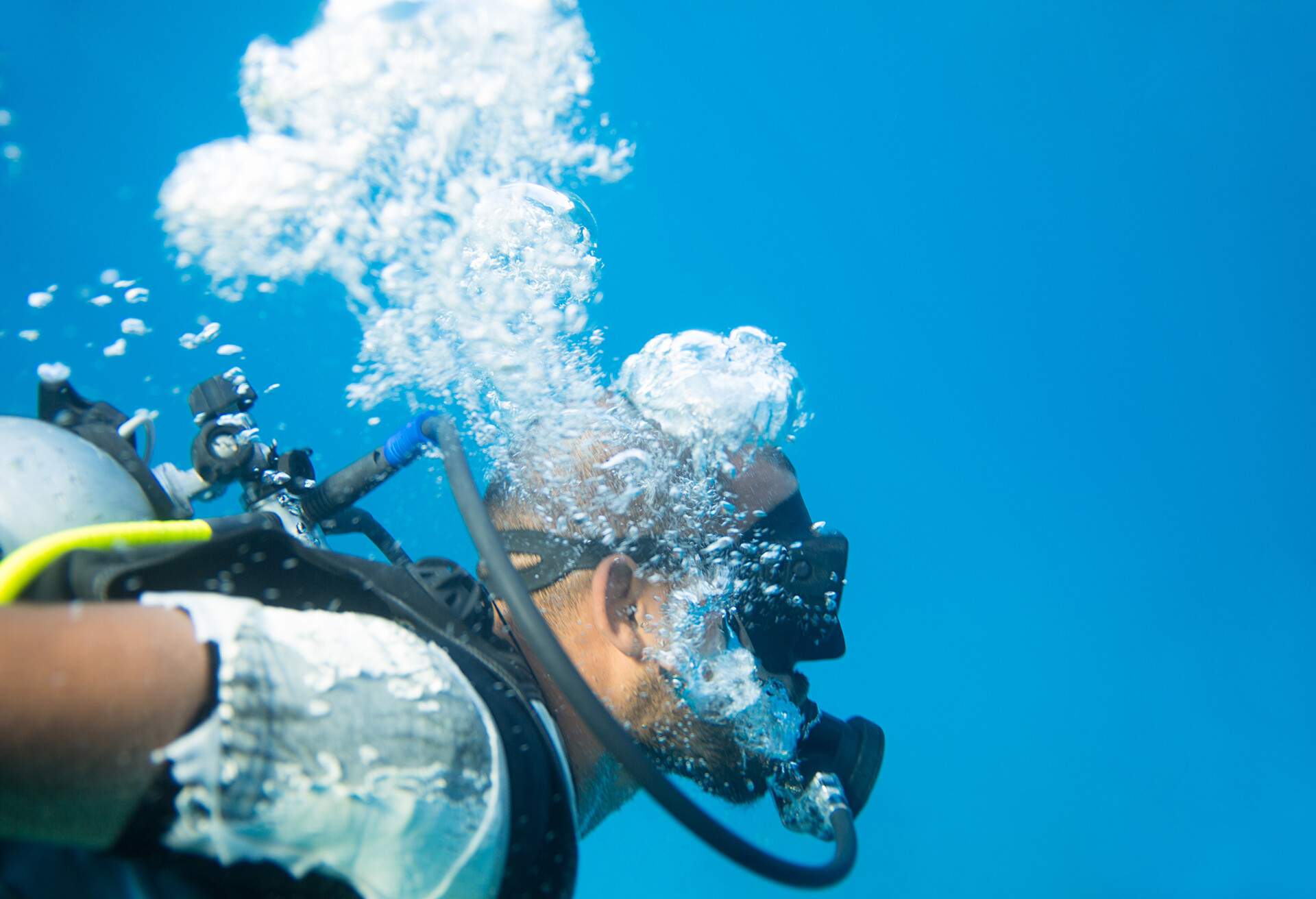 A scuba diver swims in the deep turquoise crystal clear water creating air bubbles.