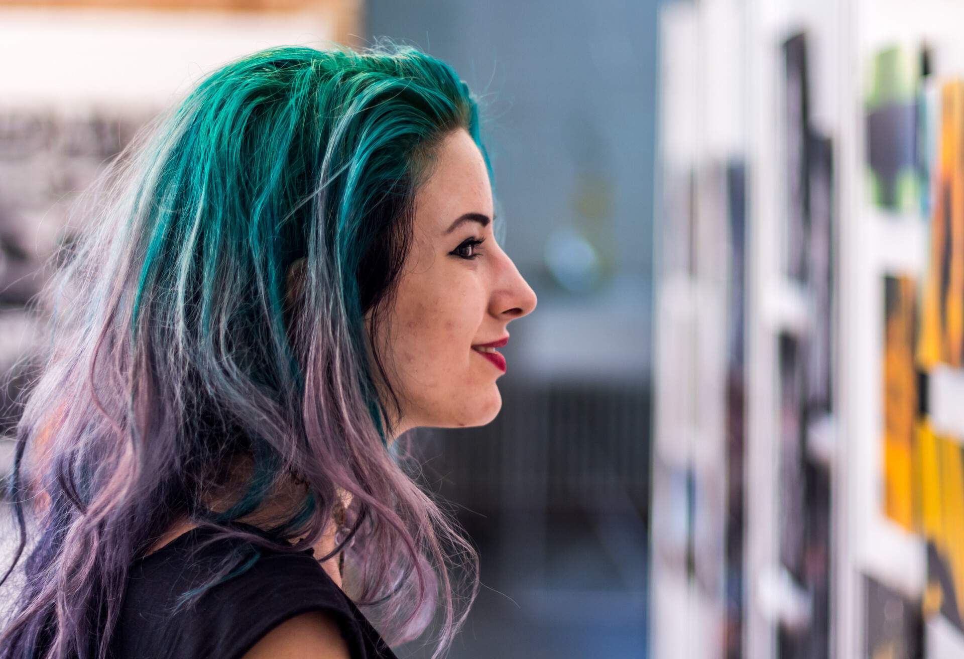 A purple-haired woman looks at artworks on the wall.