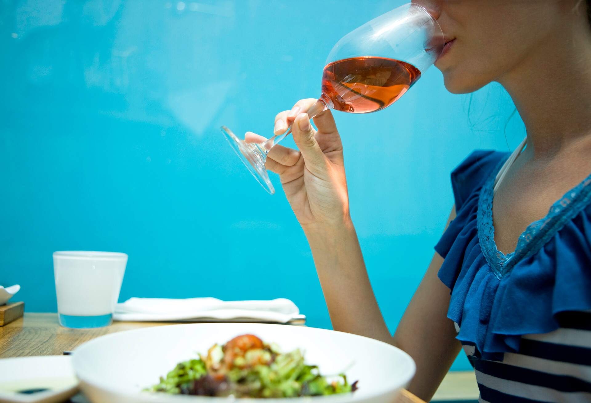 An individual with a meal and sipping from a glass of rose wine.