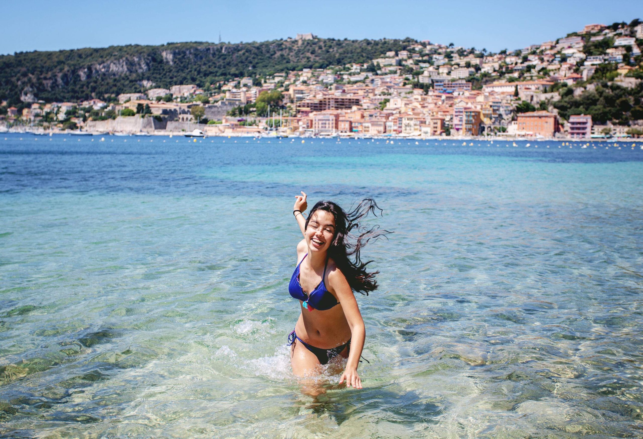 A woman in a blue bikini wading in the ocean.