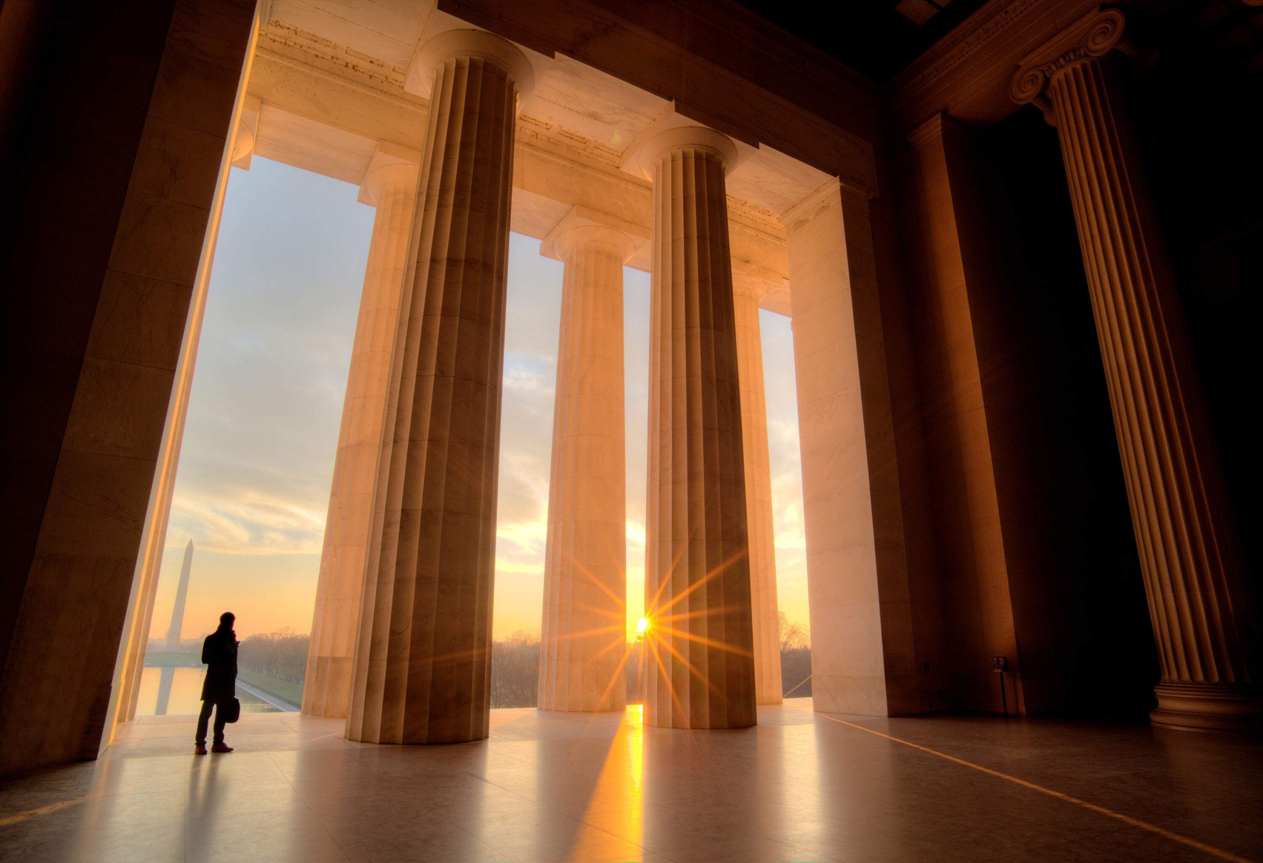 The sun's rays peeked behind the tall Doric-style columns with a lone man standing.