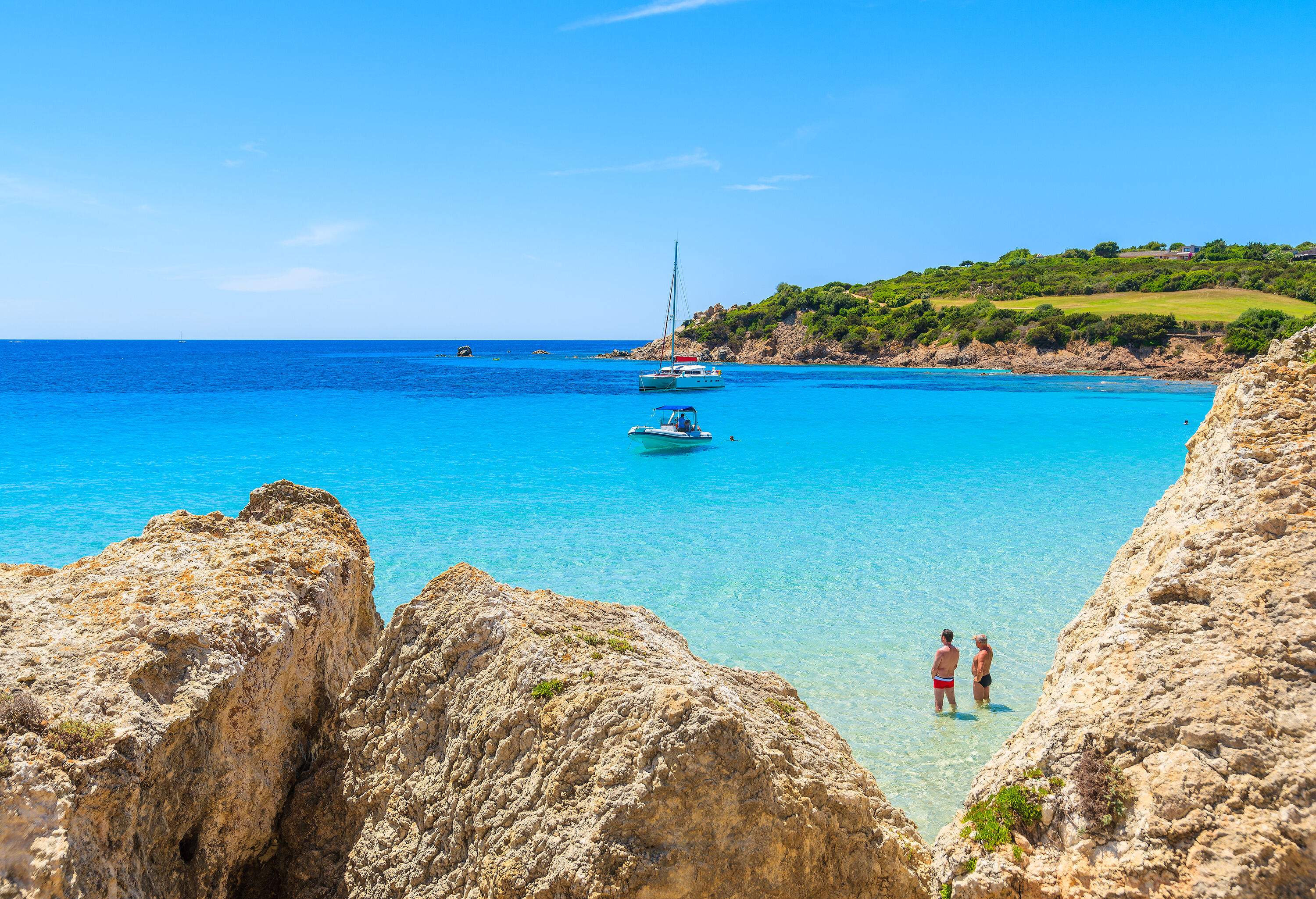 Two men knee-deep in the turquoise water, peering out into the boats in the near distance.