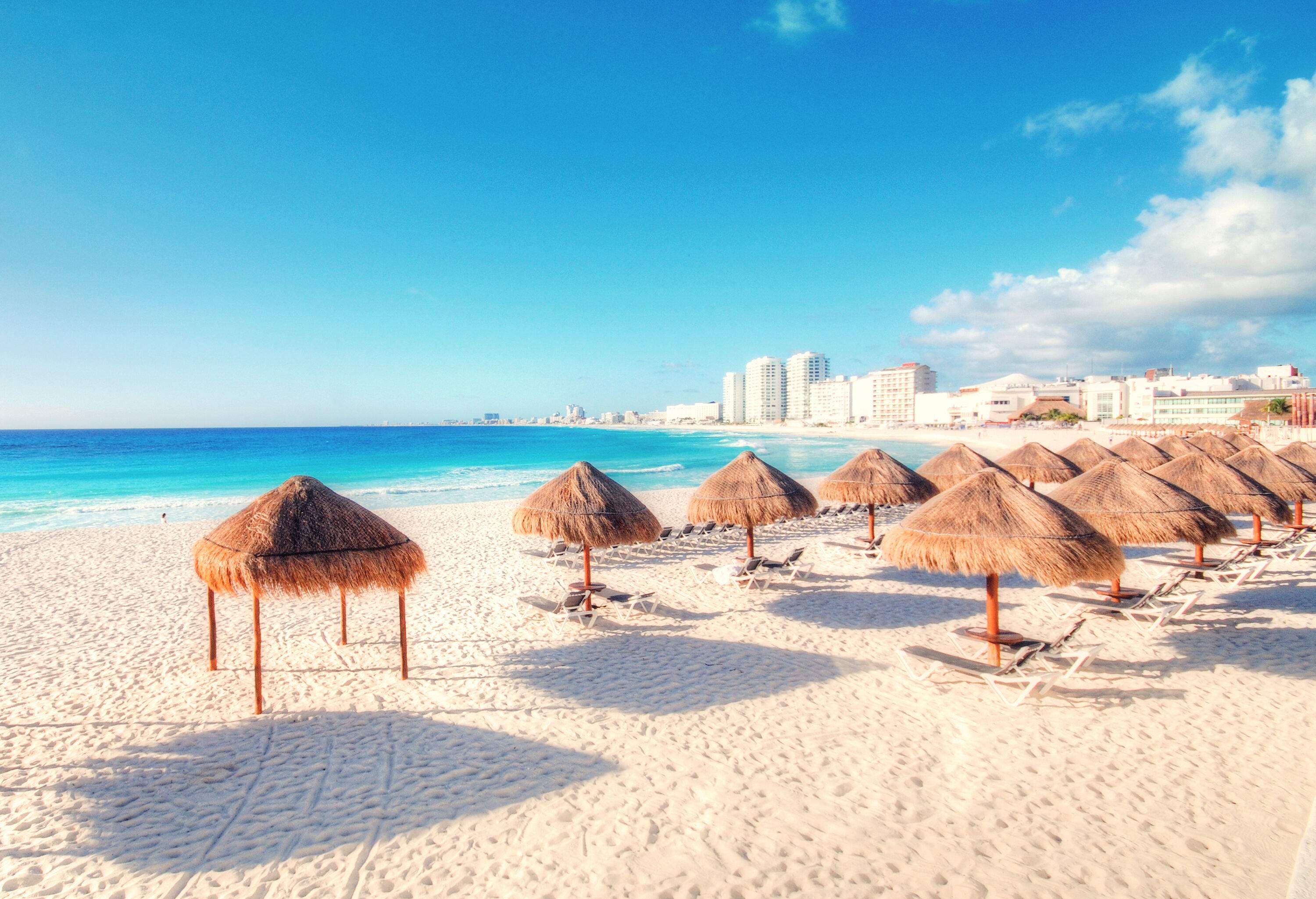 Sun loungers and thatched umbrellas lining a white beach with fine sand.