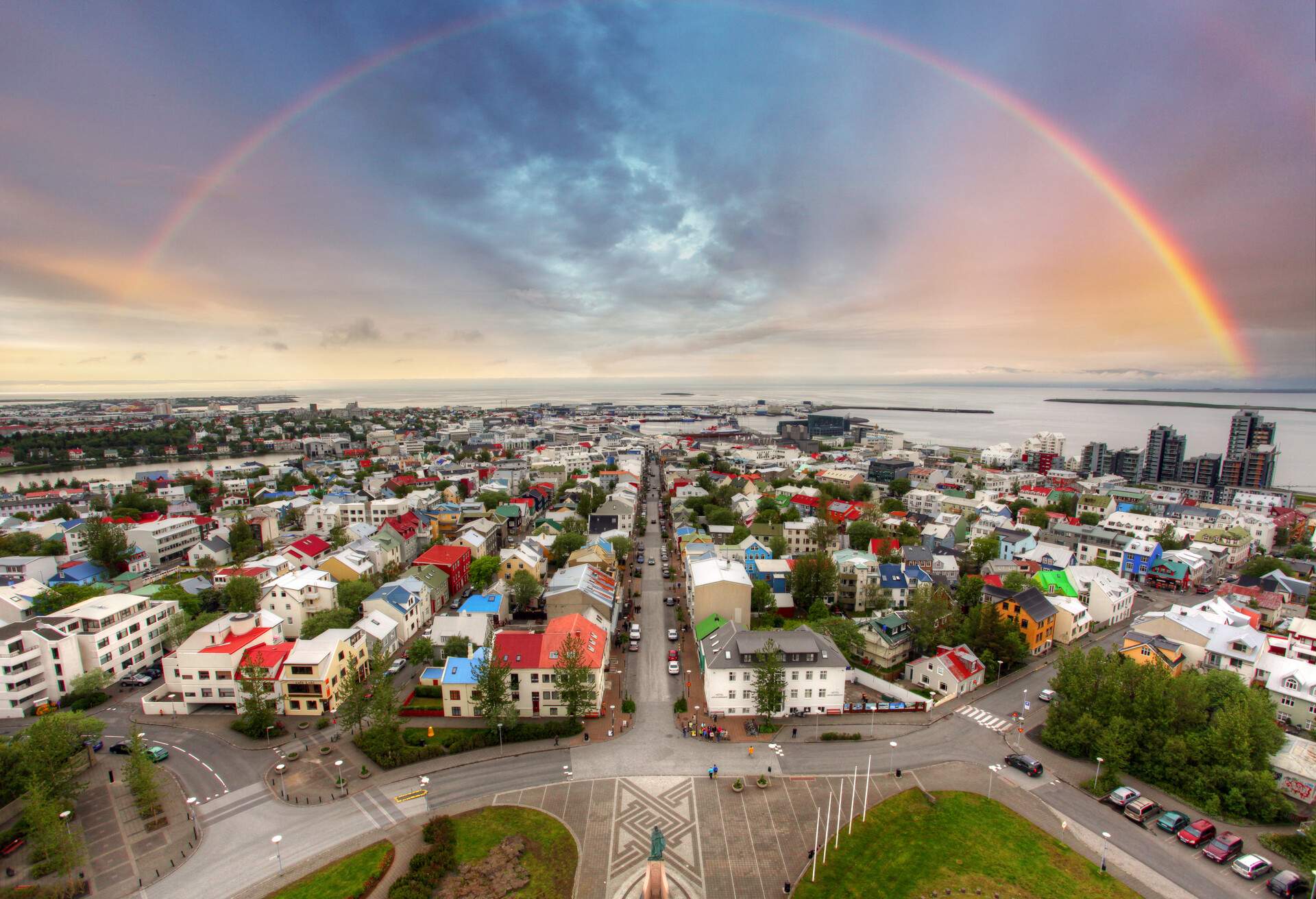 A road cuts across a residential neighbourhood in a city with a rainbow in the sky.