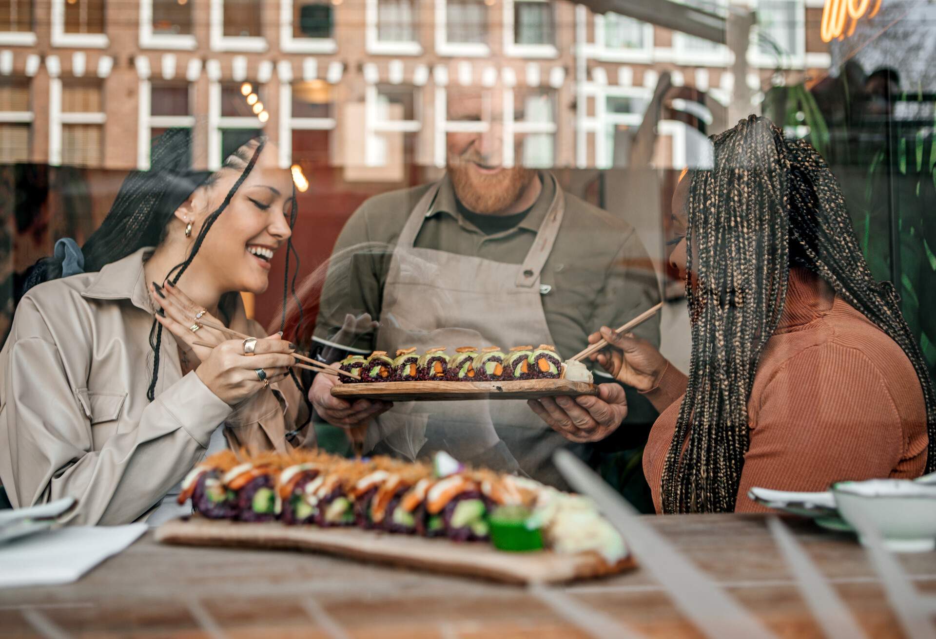 A male senior served the sushi on wooden boards to two female customers inside a restaurant.