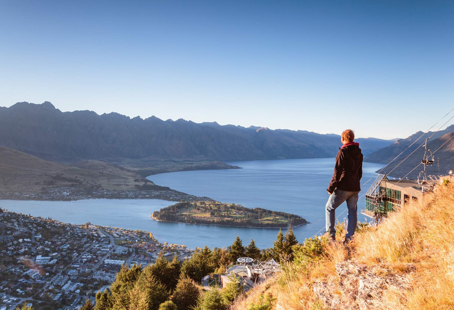 Hiker looking at Queenstown from lookout at sunrise, Otago, New Zealand