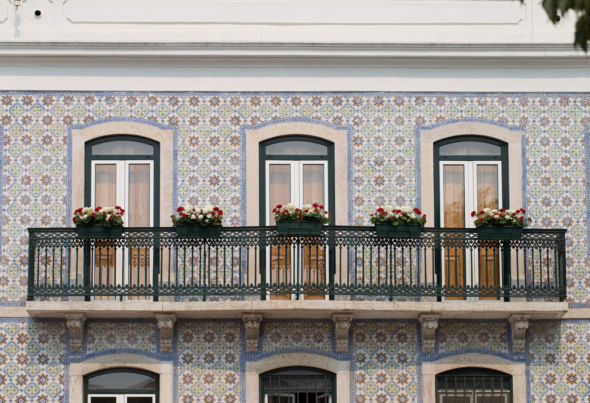 A beautiful balcony adorned with flowering plants and colourful ceramic tiles wall.
