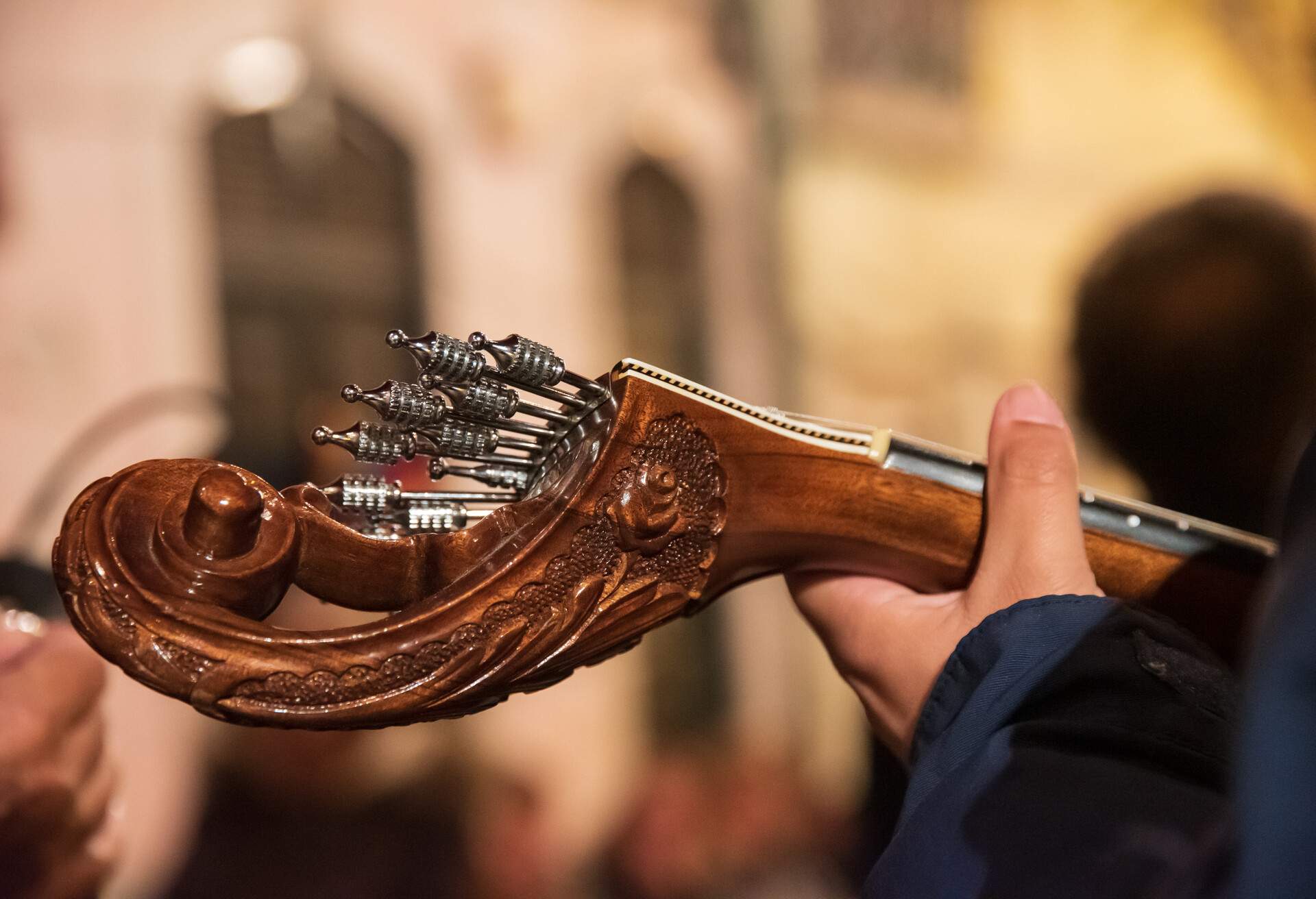 A hand strumming the strings of an intricately carved guitar.