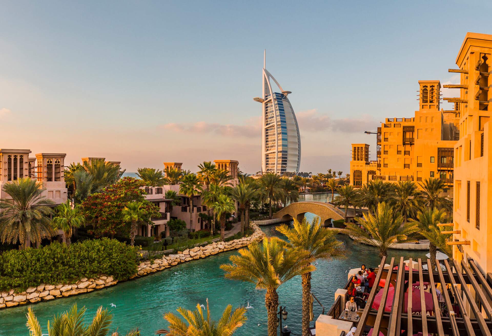 A water canal across a neighbourhood of Arab structures with wind towers and distant views of Burj Al Arab.