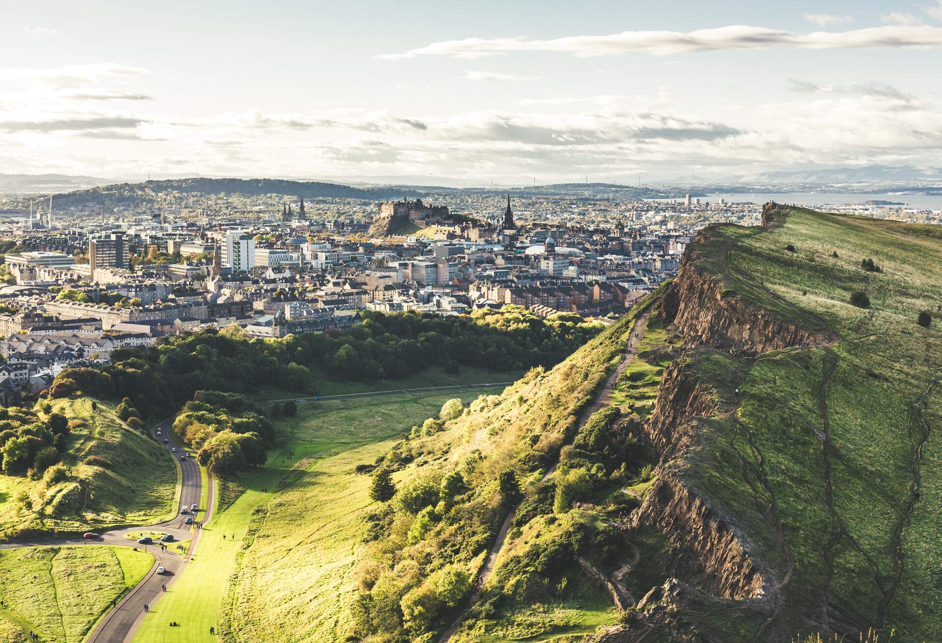 A hill with dense vegetation that rises abruptly next to a major thoroughfare and looks out over a beautiful cityscape