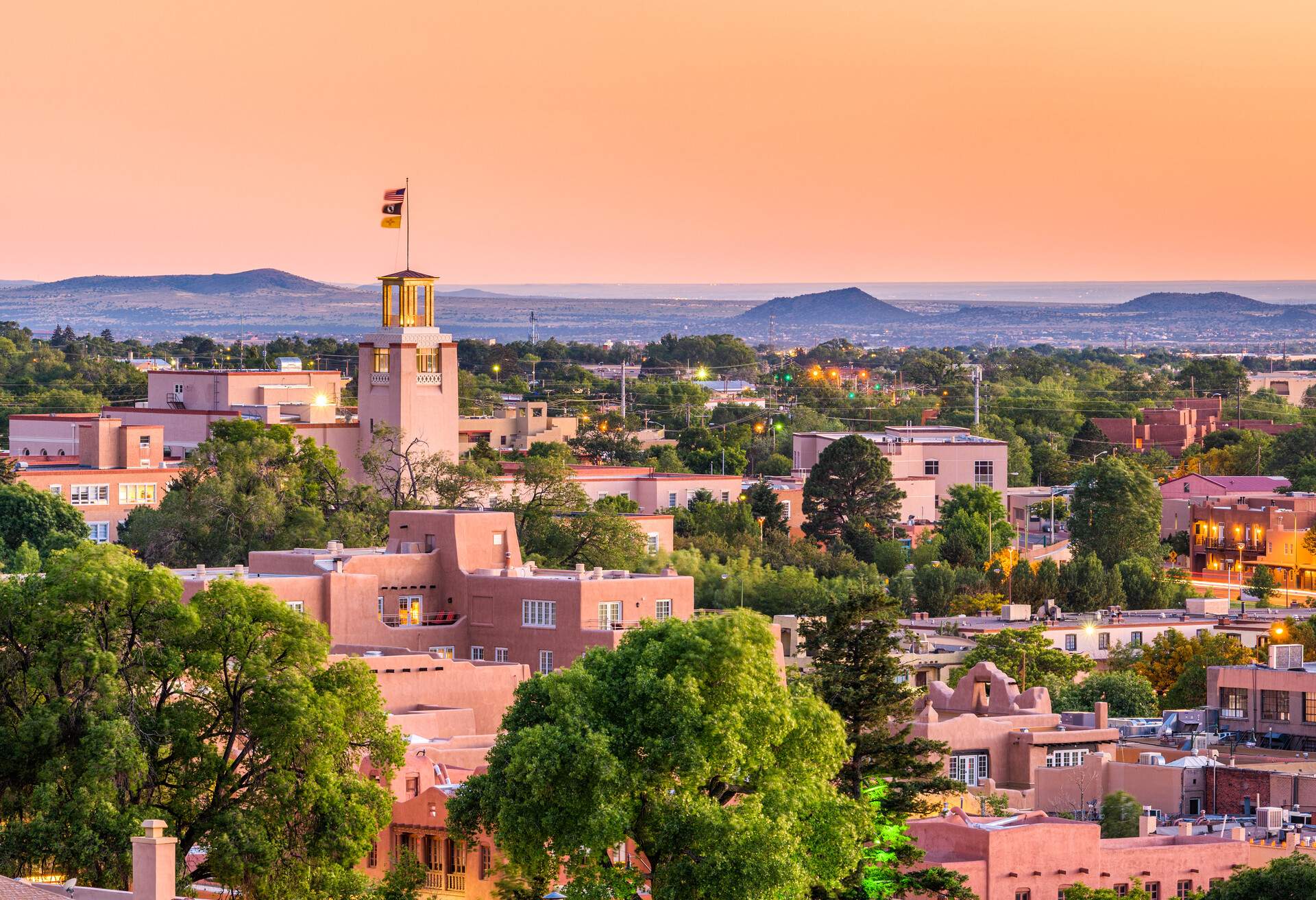 A tower with a flag overlooks a residential neighbourhood amongst lush trees under an orange sky.