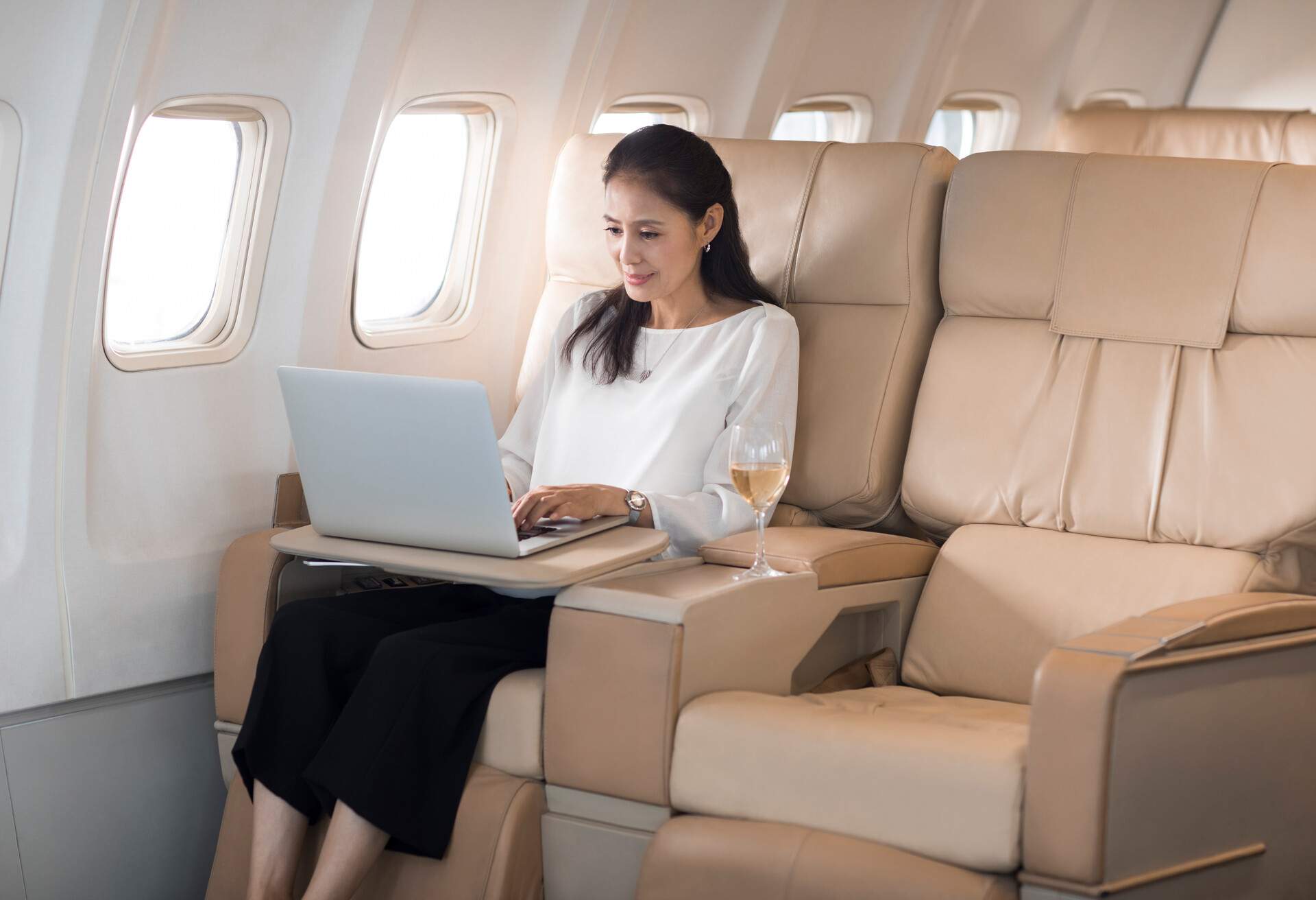 A woman working on her laptop during her flight seated on the plane's window seat.